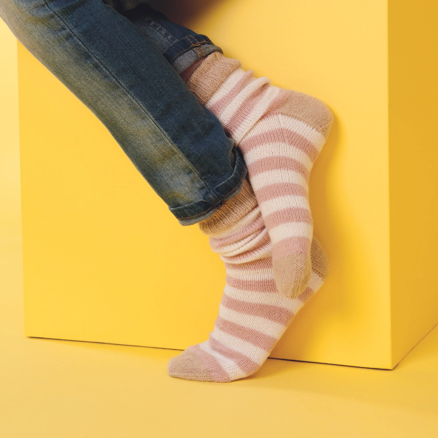 Füße, welche gestrickte Ringelsocken aus weißem und rosa Garn tragen.