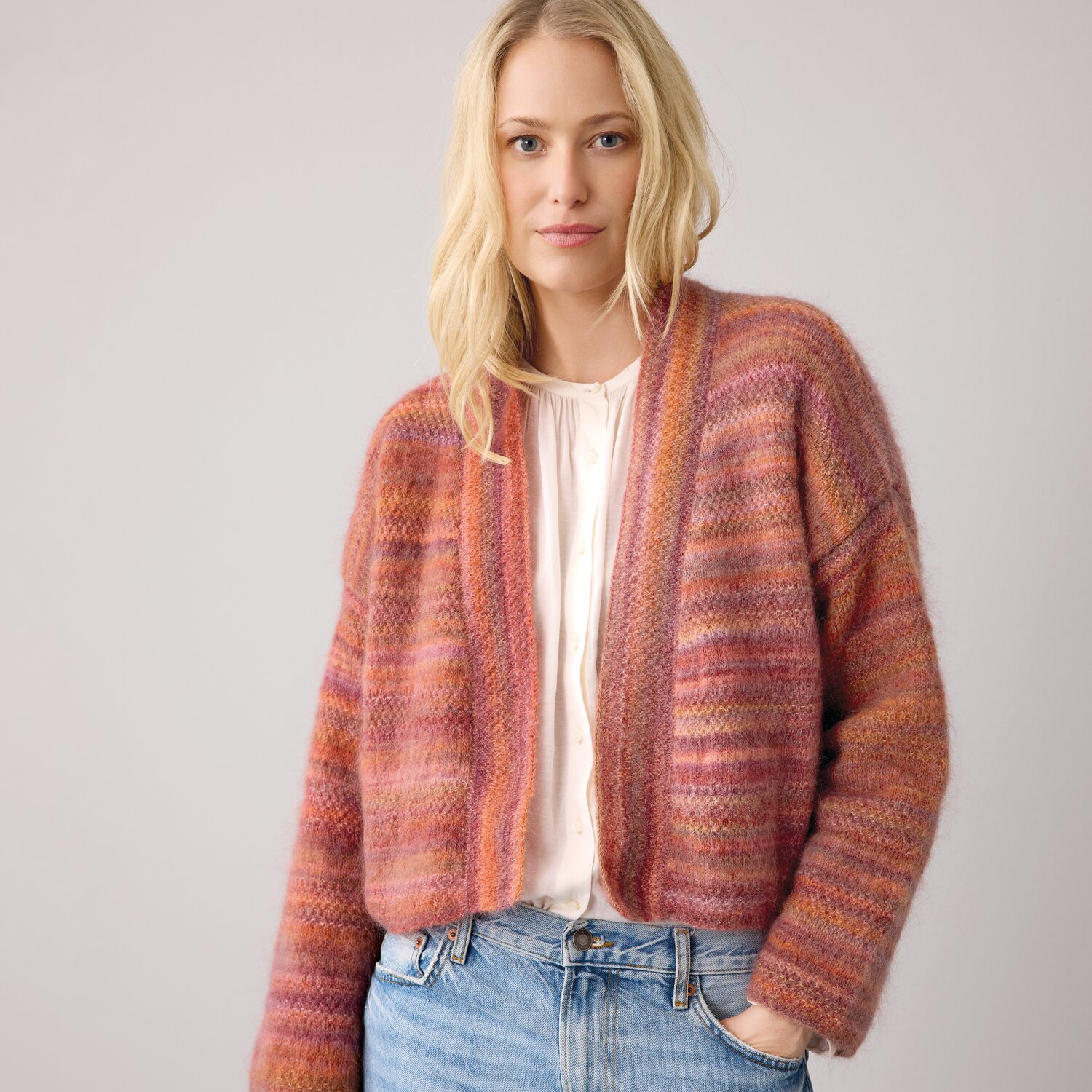 Strickset Kimono-Jacke Modell 01 aus DNM 14: Frau trägt bunte, gestreifte Jacke in warmen Tönen, kombiniert mit heller Bluse und Jeans.