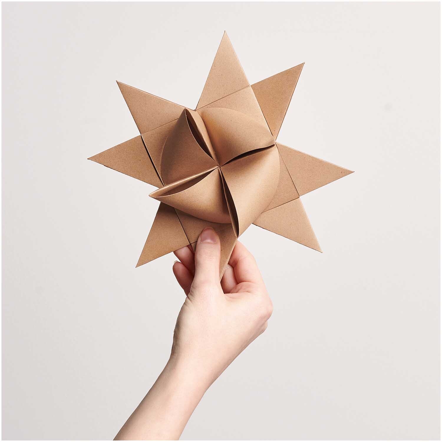 Paper Poetry Fröbelstreifen XXL 180g/m2 20 Stück: Hand hält gefalteten Stern aus Kraftpapier von Rico Design. Ideal für kreative Bastelprojekte.