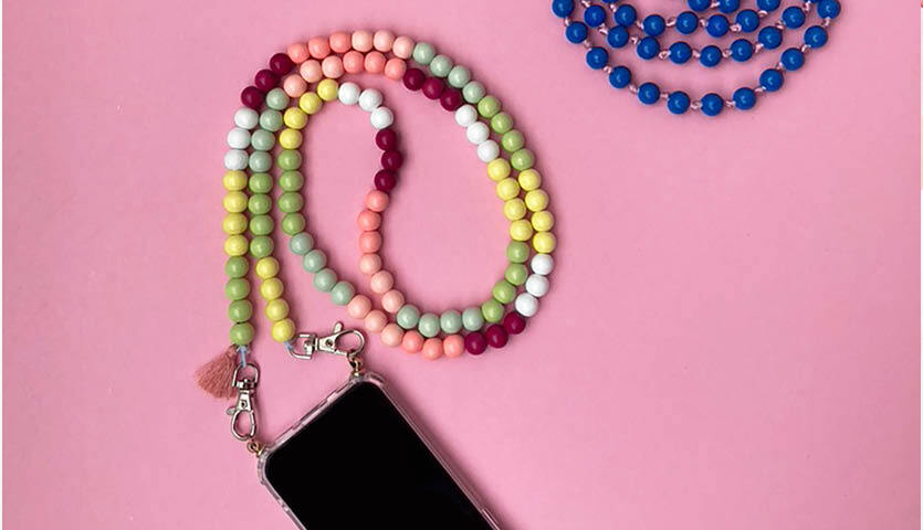 Bastelanleitung Handykette aus Holzperlen: Bunte Perlenkette mit Smartphone auf rosa Hintergrund.