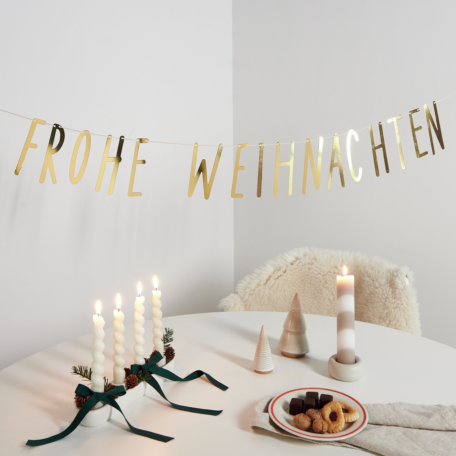 Paper Poetry Girlande Frohe Weihnachten in Gold über einem festlich gedeckten Tisch mit Kerzen und Gebäck.