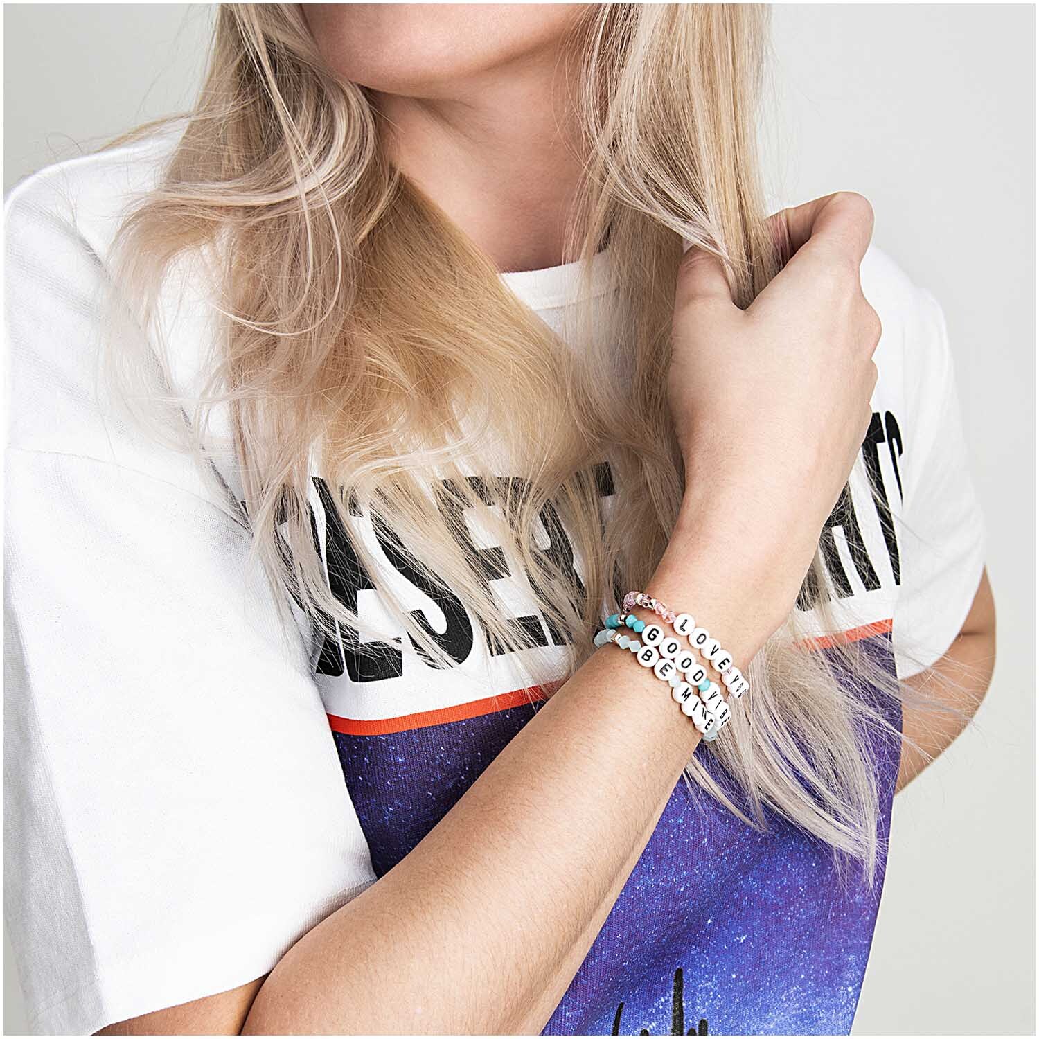 Buchstabenperle: Frau trägt Armbänder mit bunten Perlen von Rico Design, kombiniert mit weißem T-Shirt.