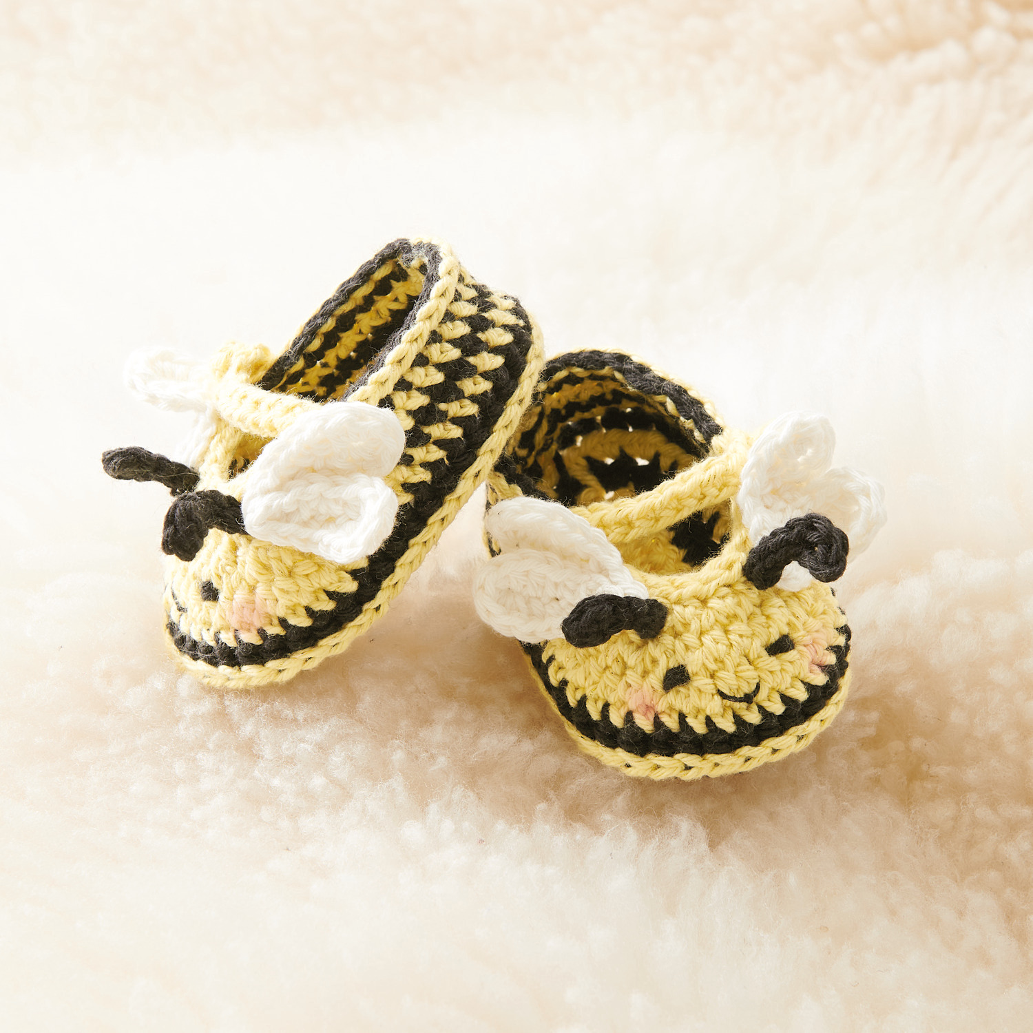 Ricorumi Häkelset Baby Booties Biene: Niedliche gehäkelte Babyschuhe in Bienenform auf weichem Hintergrund.