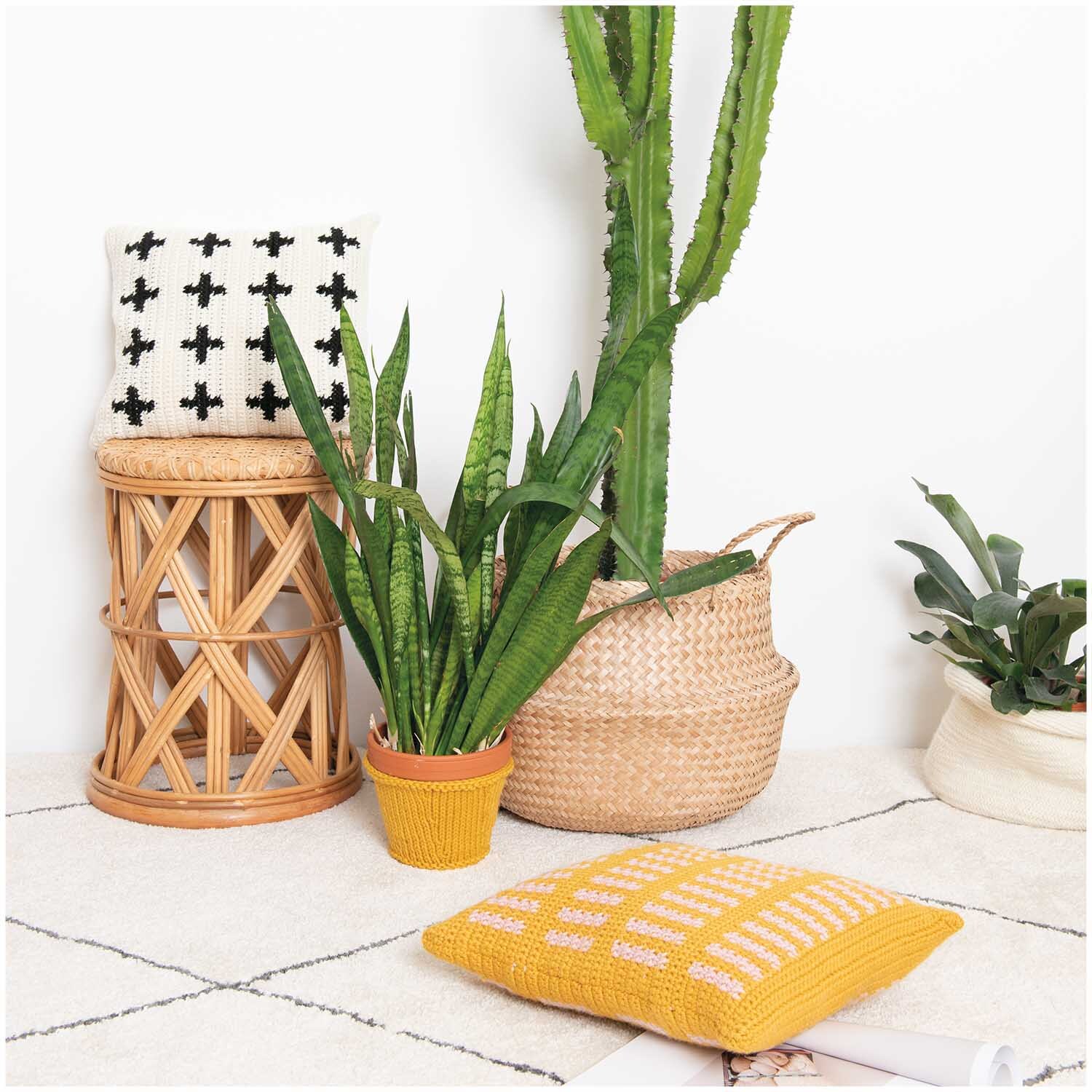 Essentials Mega Wool chunky: Senffarbene Kissen aus Rico Design Wolle, dekoriert mit Pflanzen auf einem Teppich.