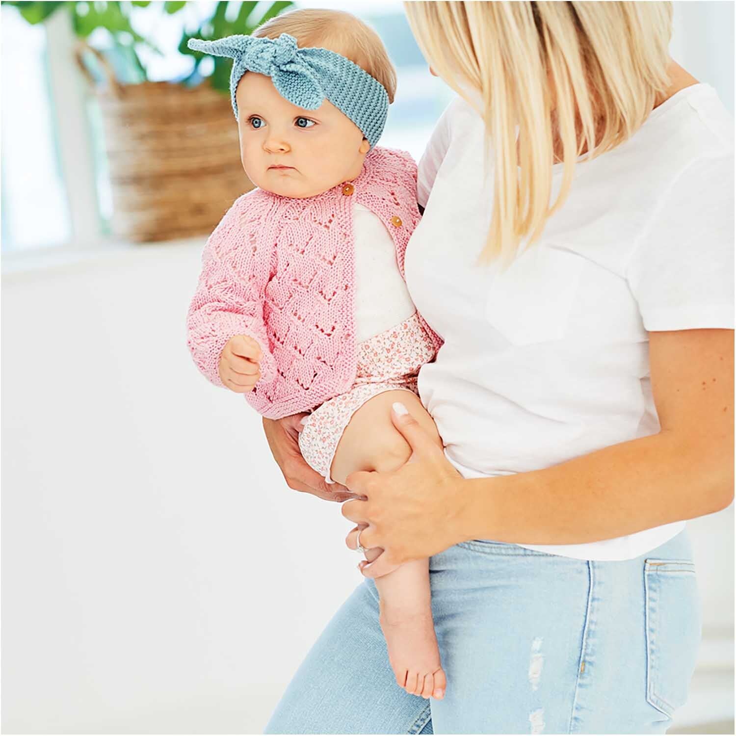 Rico Baby Cotton Soft dk: Frau hält Baby in rosa Strickjacke, blauem Stirnband, helle Umgebung.