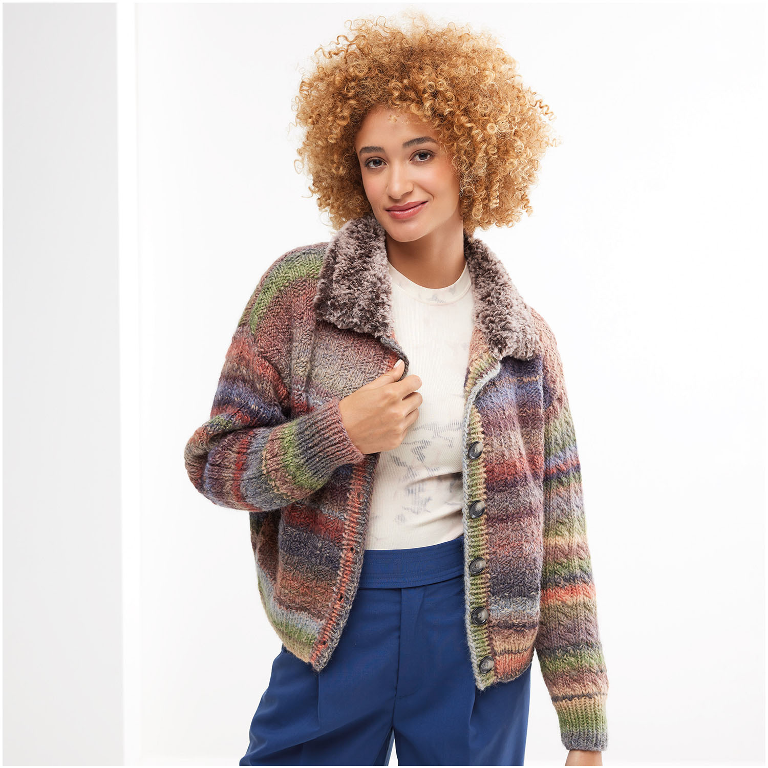 Strickset Jacke Modell 33: Bunte, gestrickte Jacke mit Kragen, getragen von Frau in blauer Hose.