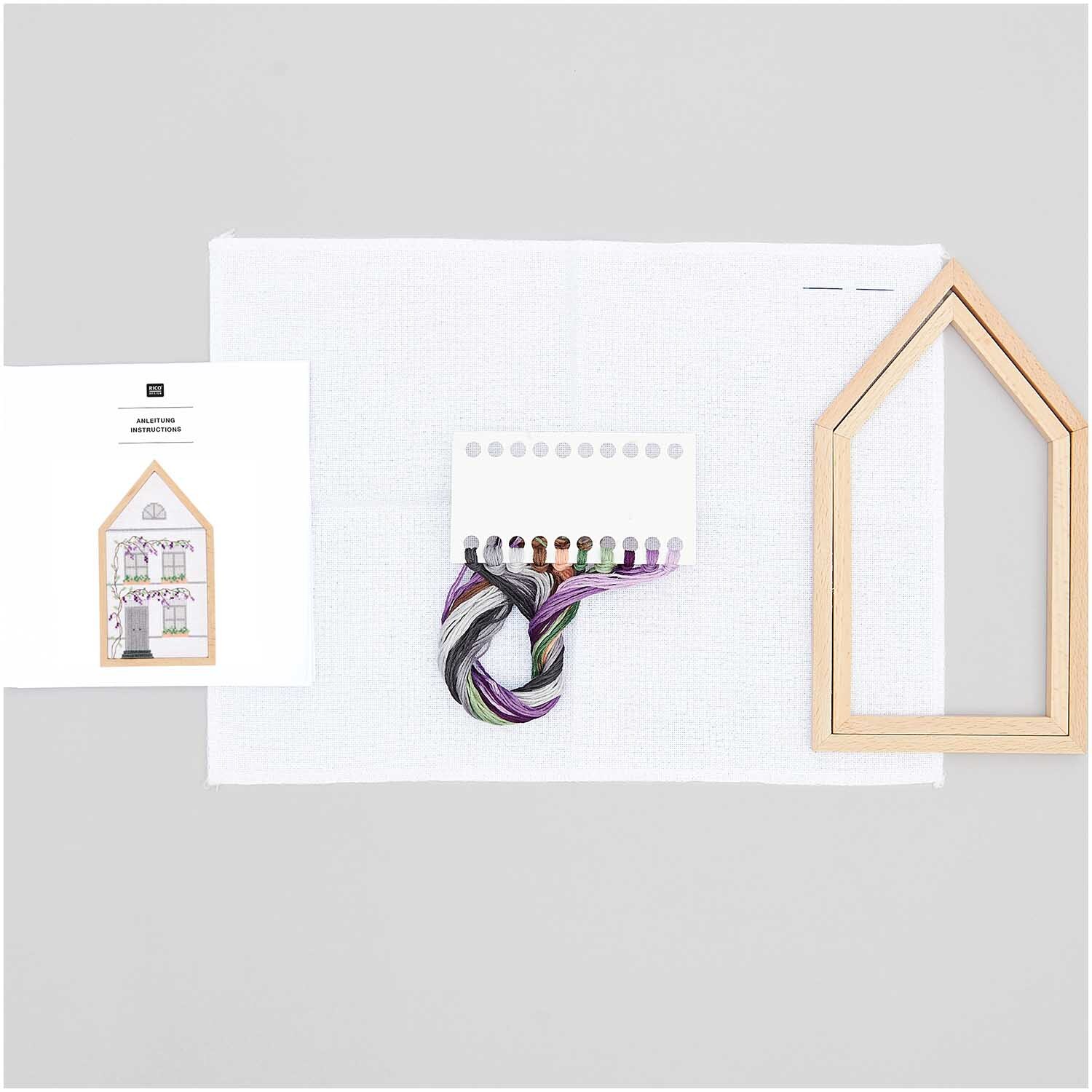 Stickpackung Sommerhaus mittel von Rico Design mit Holzrahmen, Garn und Anleitung auf weißem Hintergrund.