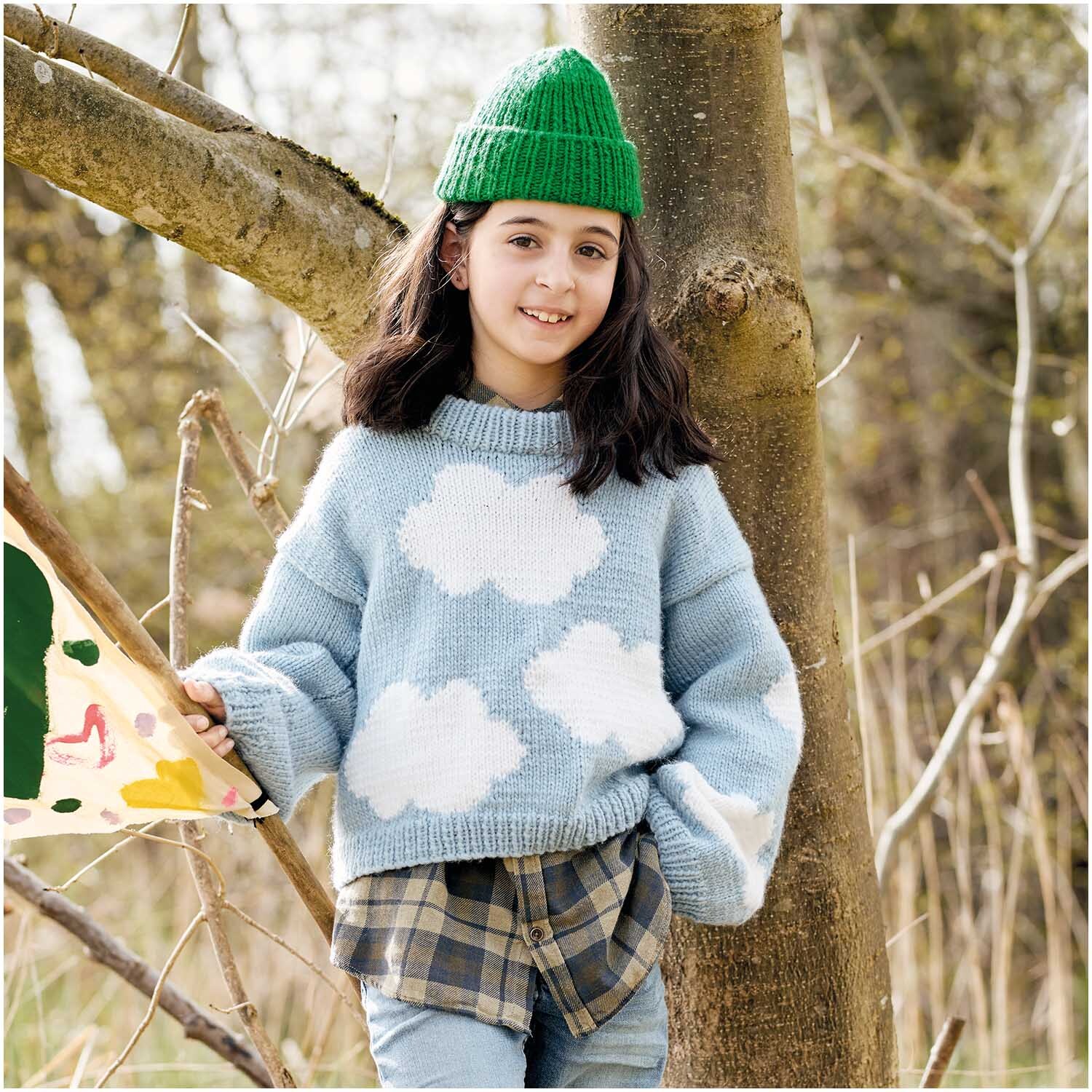 Essentials Super aran Pullover in Hellblau mit Wolkenmuster, getragen von einem Mädchen im Freien.