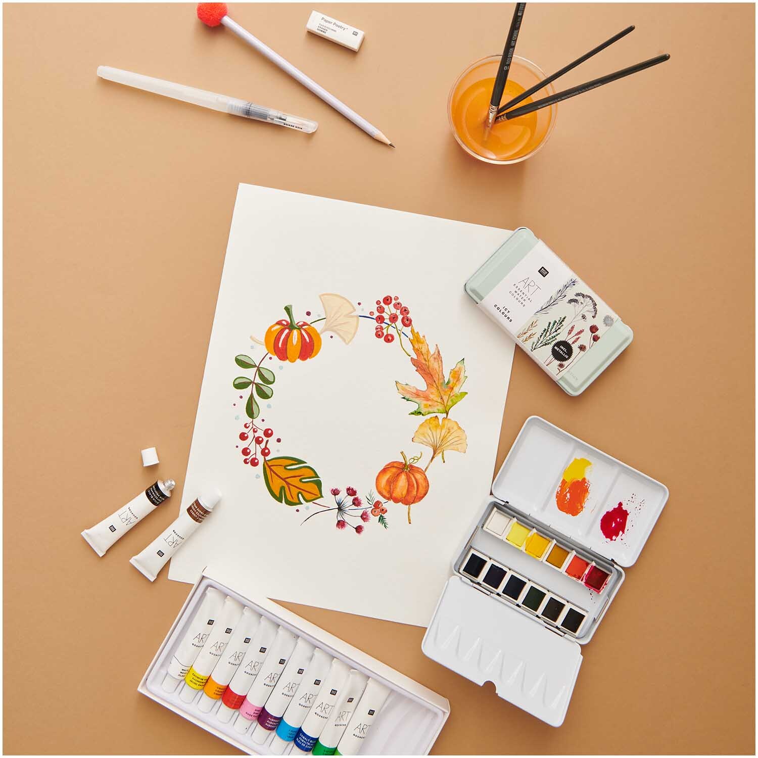 ART Essential Aquarellfarben Icy Colours 12 Farben von Rico Design, arrangiert mit Pinseln und herbstlichem Kunstwerk auf braunem Hintergrund.