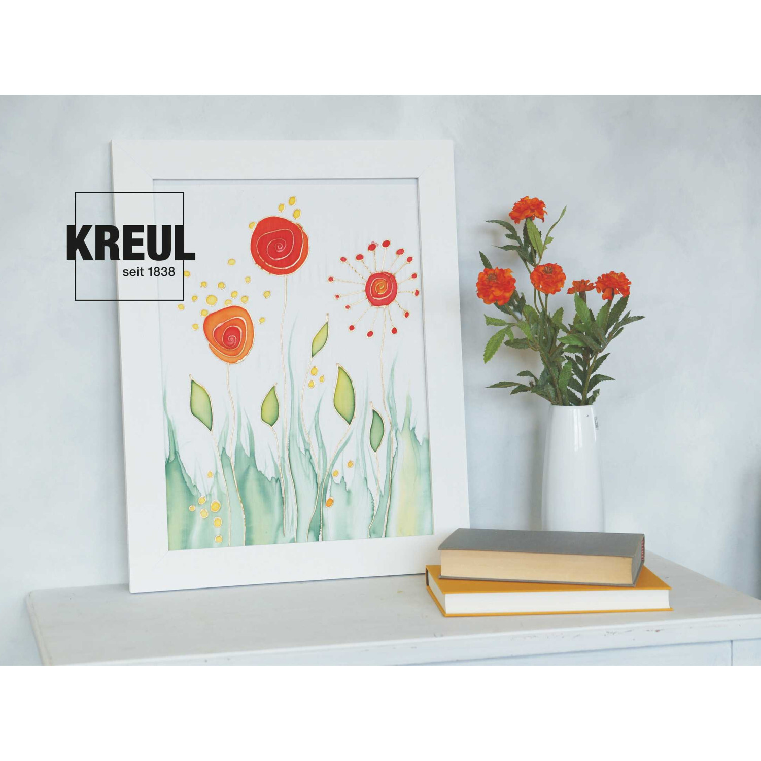 Javana Malen auf Seide Starterset: Buntes Blumenbild in weißem Rahmen, daneben Vase mit roten Blumen auf Tisch.