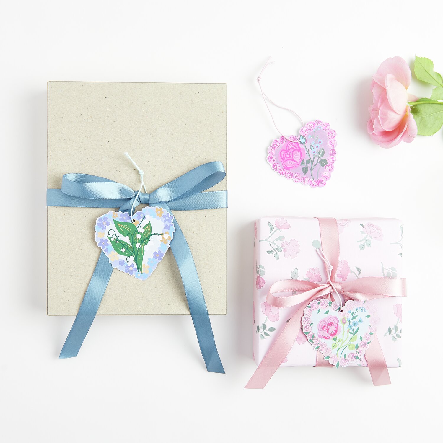 Paper Poetry Geschenkanhänger La Vie en Rose Herzen, 9 Stück, dekorieren zwei Geschenke mit blauen und rosa Bändern auf hellem Hintergrund.