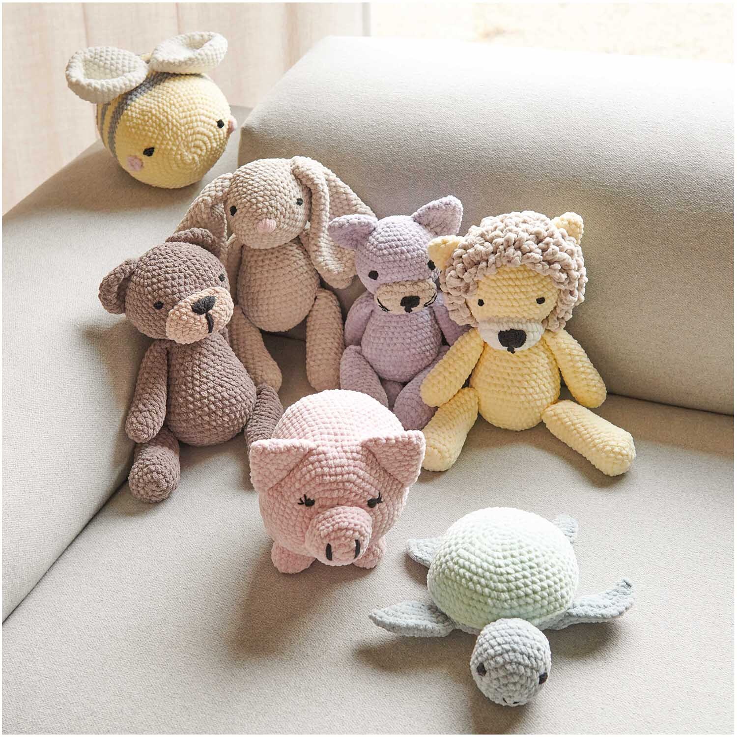 Creative Chenillove: Eine Sammlung gehäkelter Tiere auf einem Sofa, darunter Bär, Schwein und Löwe. Ideal für kreative Projekte.