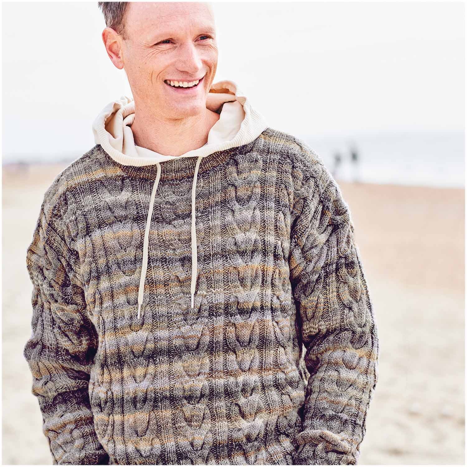 Creative Melange aran Wonderball: Mann in gestricktem Pullover am Strand, lächelnd, in Naturtönen.