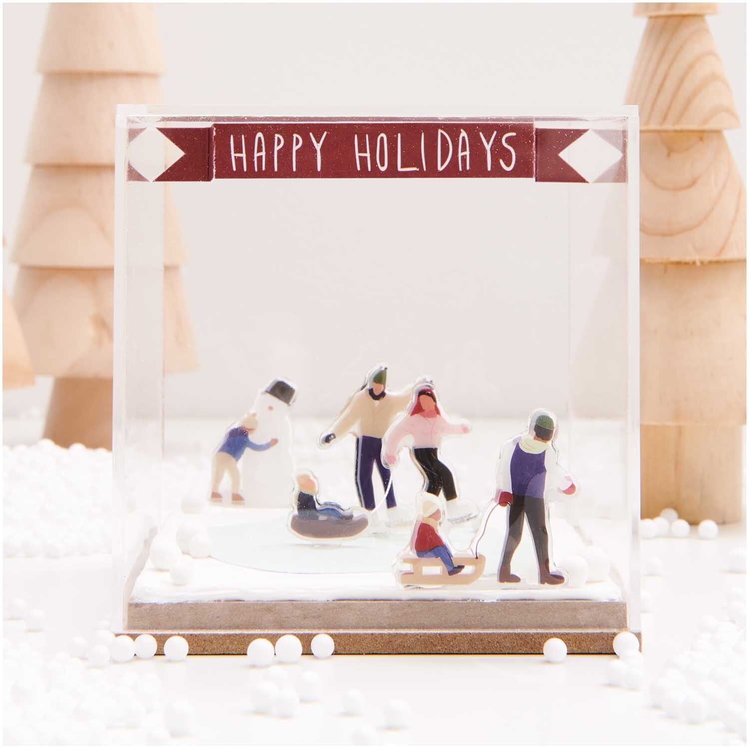 Figurico Modelliermasse 28g: Miniatur-Szene mit Menschen beim Wintersport in Schneelandschaft, dekoriert mit "Happy Holidays"-Banner.