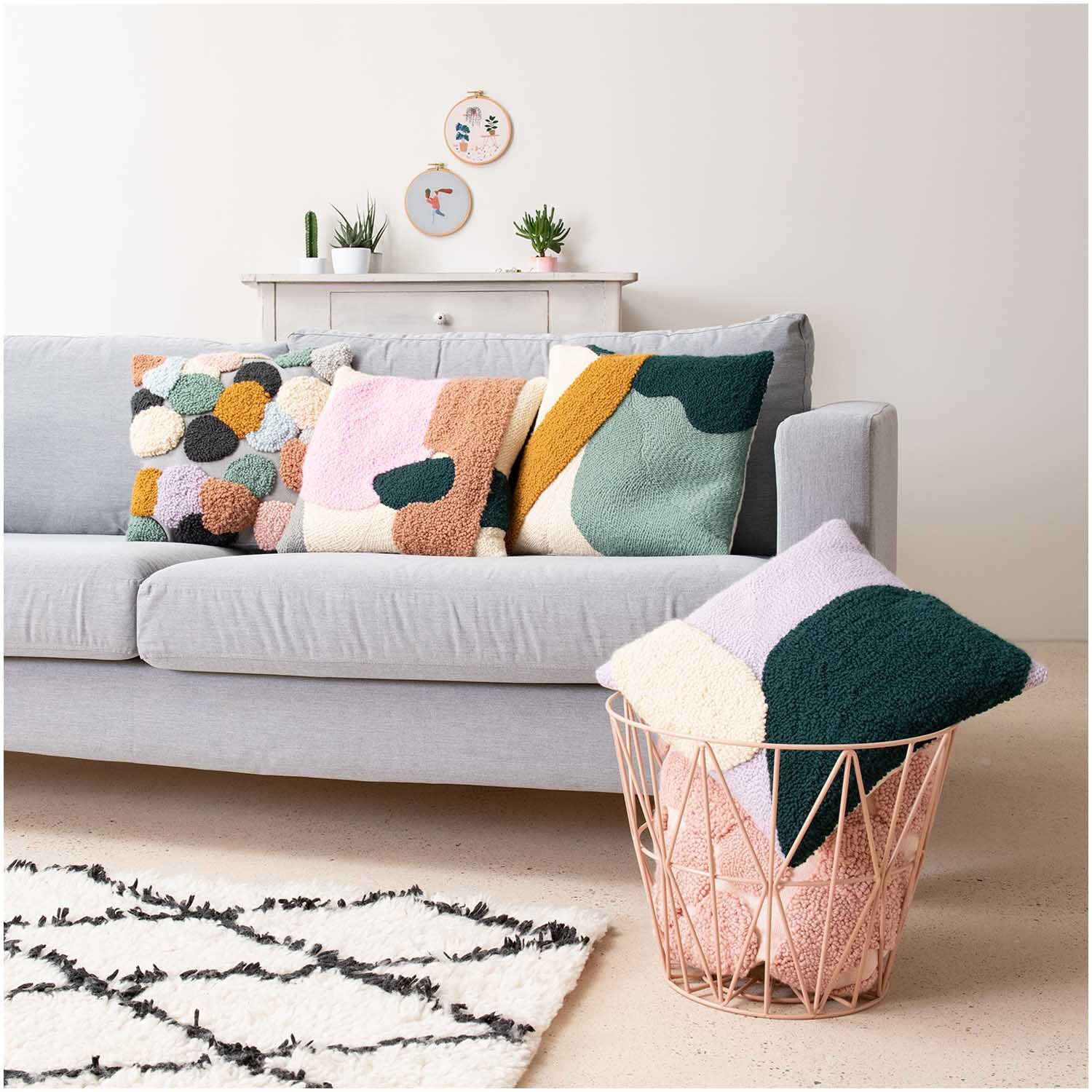 Punch Needle Packung Kissen senf-grün von Rico Design auf grauem Sofa, dekoriert mit bunten Kissen und Pflanzen im Hintergrund.