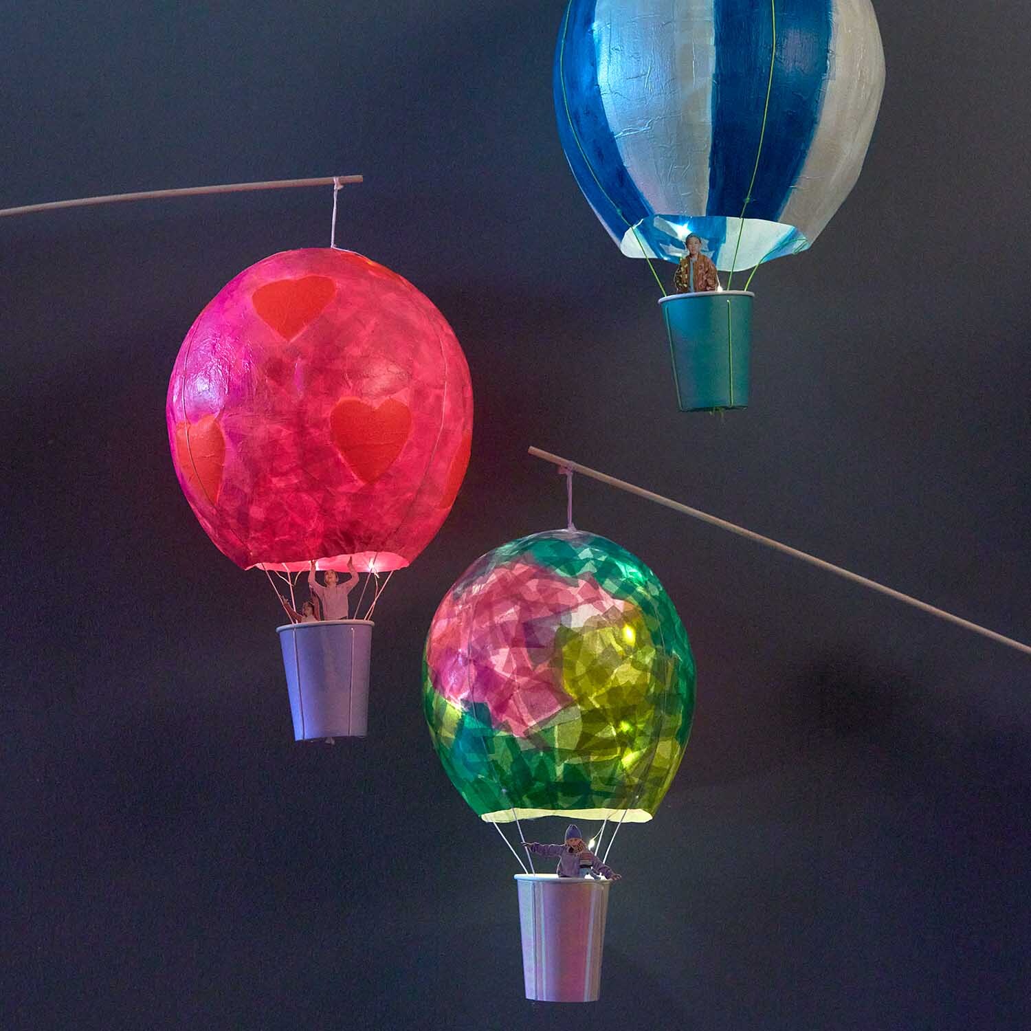 Bastelanleitung Heißluftballon-Laterne: Bunte Laternen in Rot, Blau und Grün schweben vor dunklem Hintergrund.
