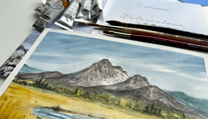 Anleitung Landschaftsbild @draw_better mit HORADAM Naturals: Aquarellfarben, Pinsel und Landschaftsgemälde auf einem Tisch arrangiert.