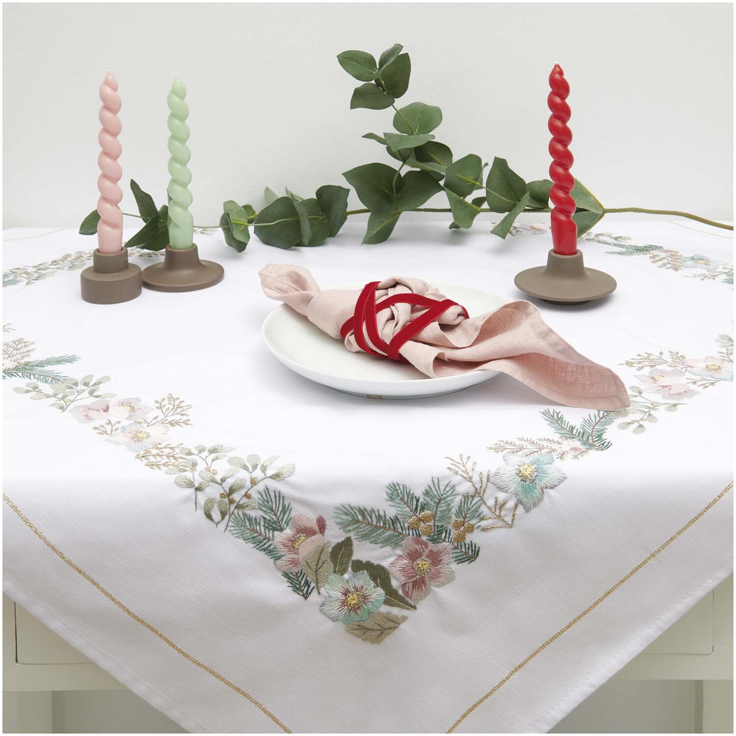 Stickpackung Tischdecke Christrosen 90x90cm mit floralen Mustern, dekoriert mit Kerzen und Eukalyptus. Ideal für festliche Anlässe.