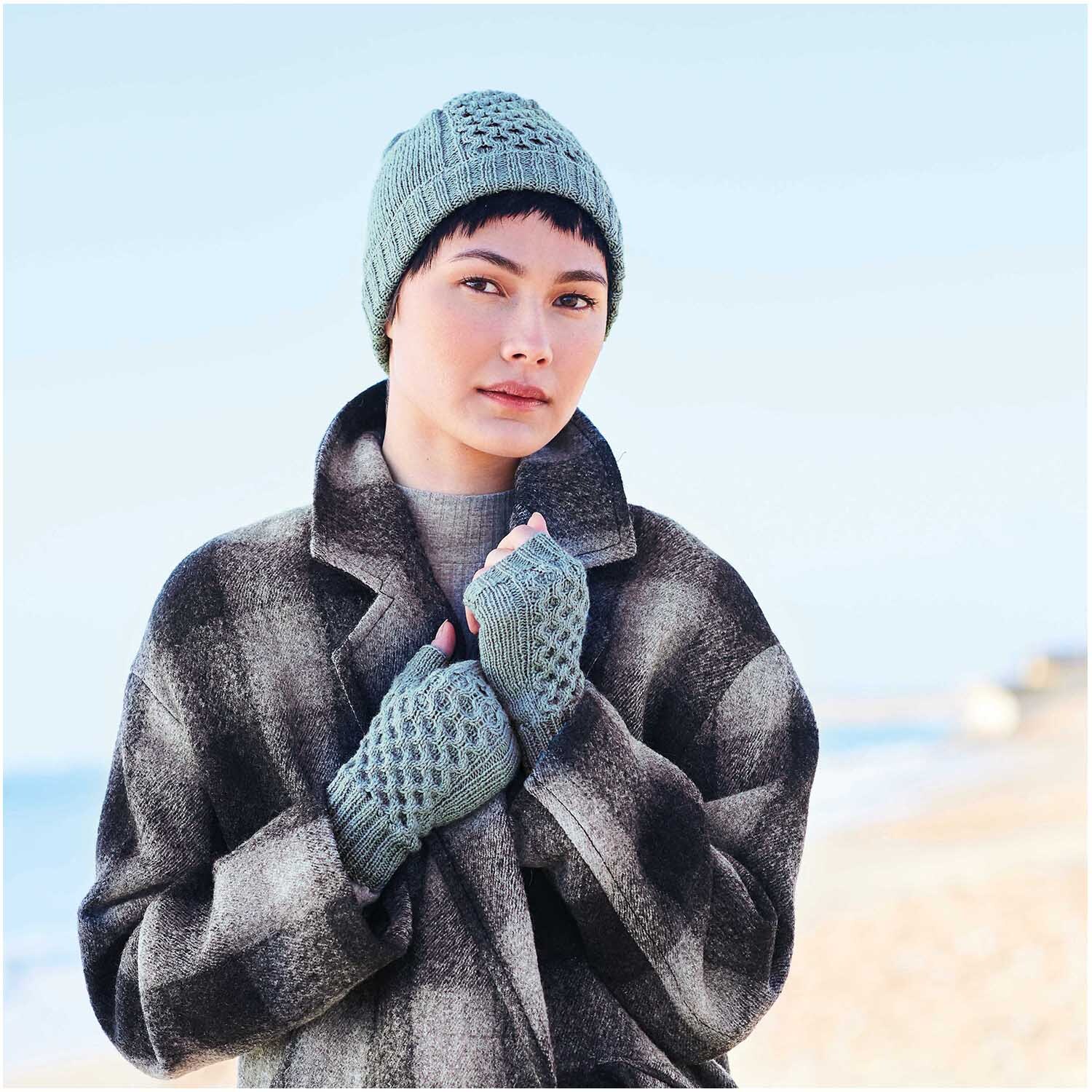 Essentials Fine Fine Merino: Person am Strand trägt gestrickte Mütze und Handschuhe in Aqua.