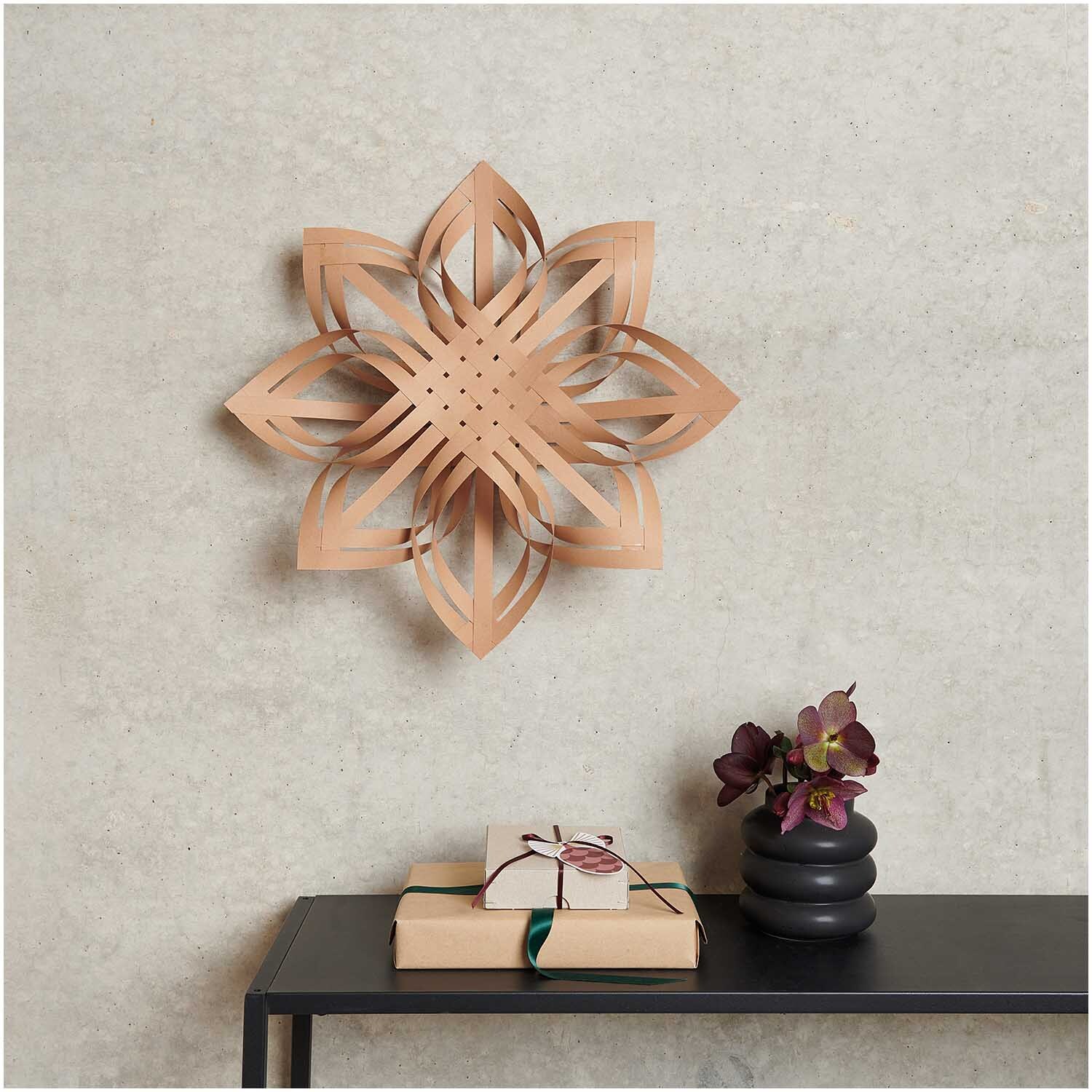 Paper Poetry Web-Stern Größe M aus Kraftpapier von Rico Design, an einer Wand hängend, dekoriert einen Raum mit einem Tisch und Geschenken.