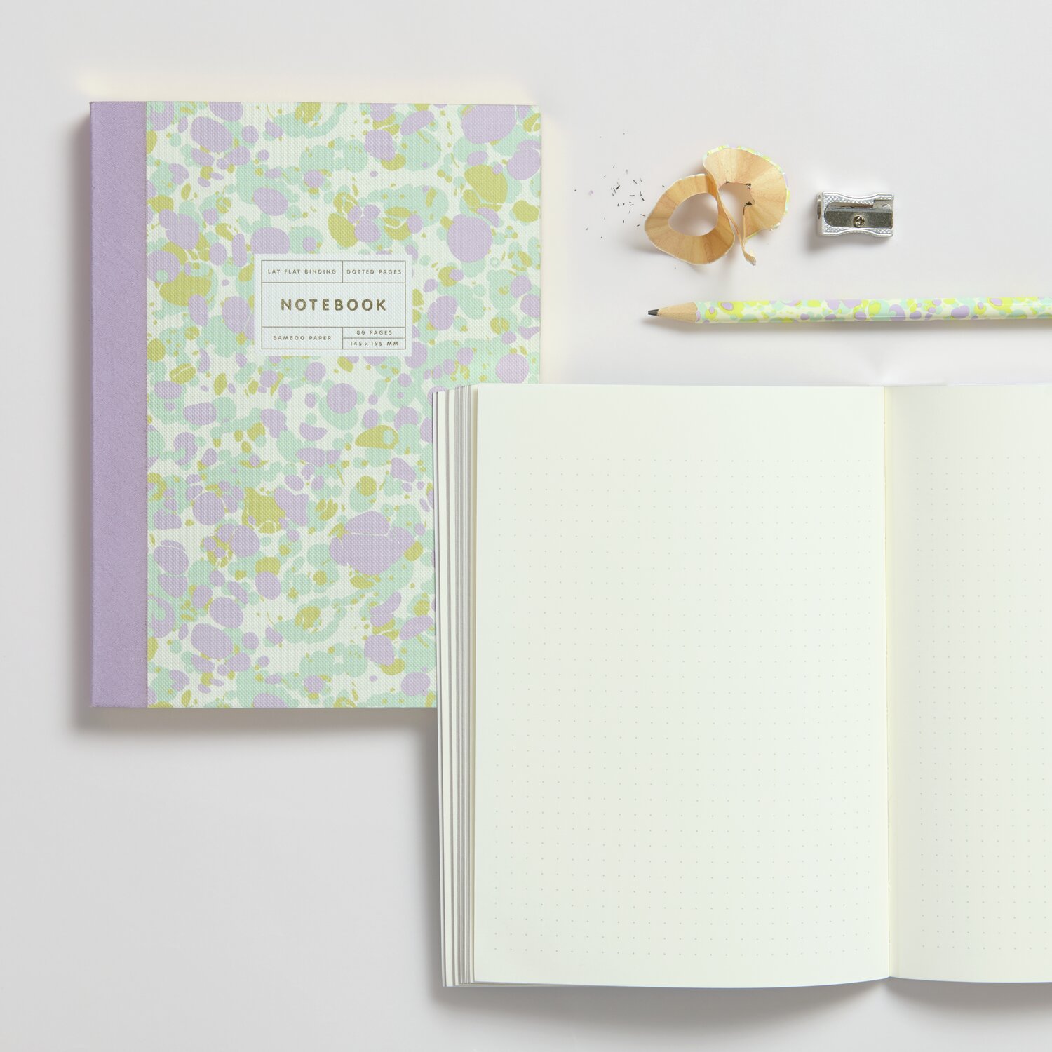 Notizbuch S Marbled 80 Seiten mit lila Rücken, offen gezeigt. Daneben Bleistift, Anspitzer und Radiergummi.