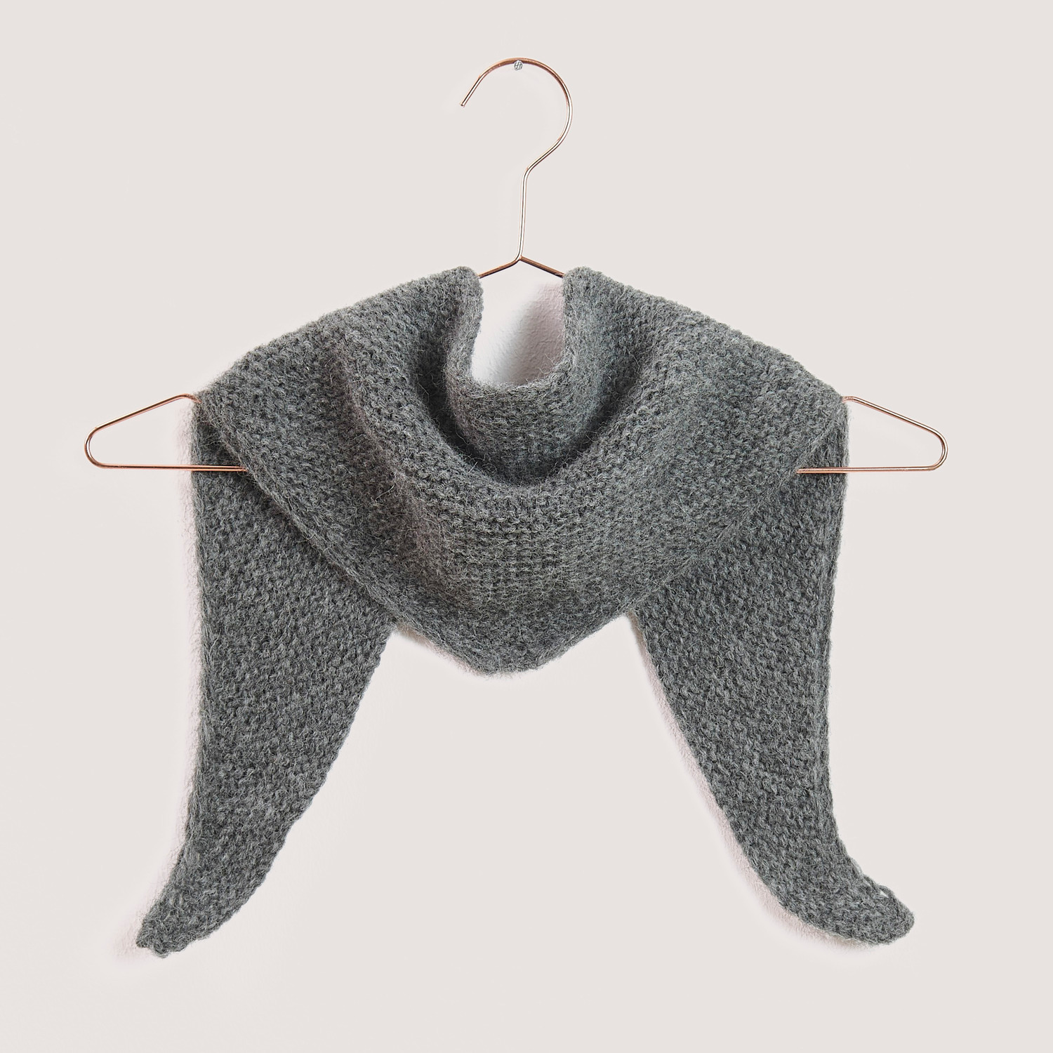 Strickset Mini Dreieckstuch Modell 09a von Rico Design in Grau, aufgehängt an einem Kleiderbügel. Ideal für stilvolle Handarbeitsprojekte.