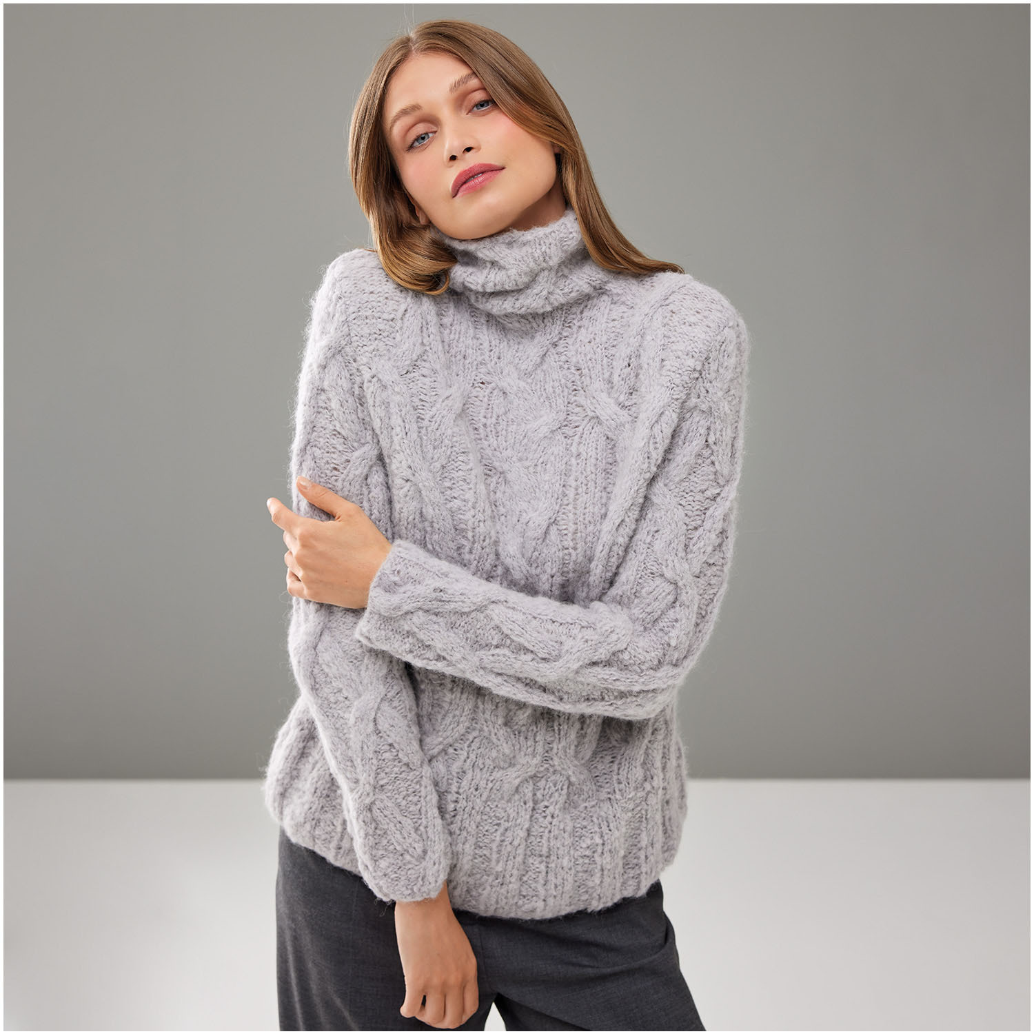 Strickset Pullover Modell 28 aus Die Neue Masche Nr. 8, grauer Rollkragenpullover mit Zopfmuster, getragen von Frau vor grauem Hintergrund.
