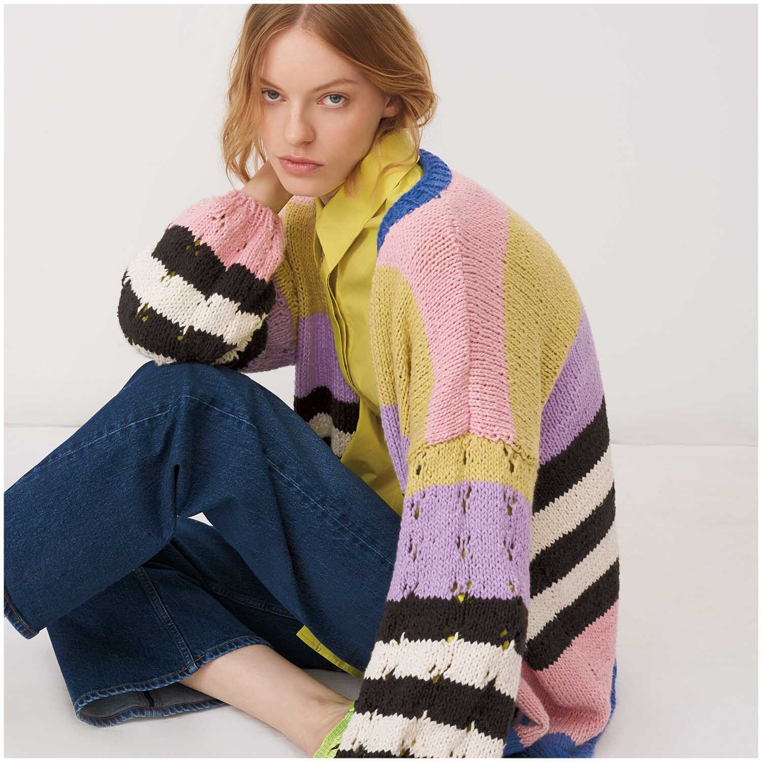 Creative So Cool + So Soft Cotton chunky: Frau in bunter Strickjacke mit Streifenmuster, sitzt auf dem Boden.