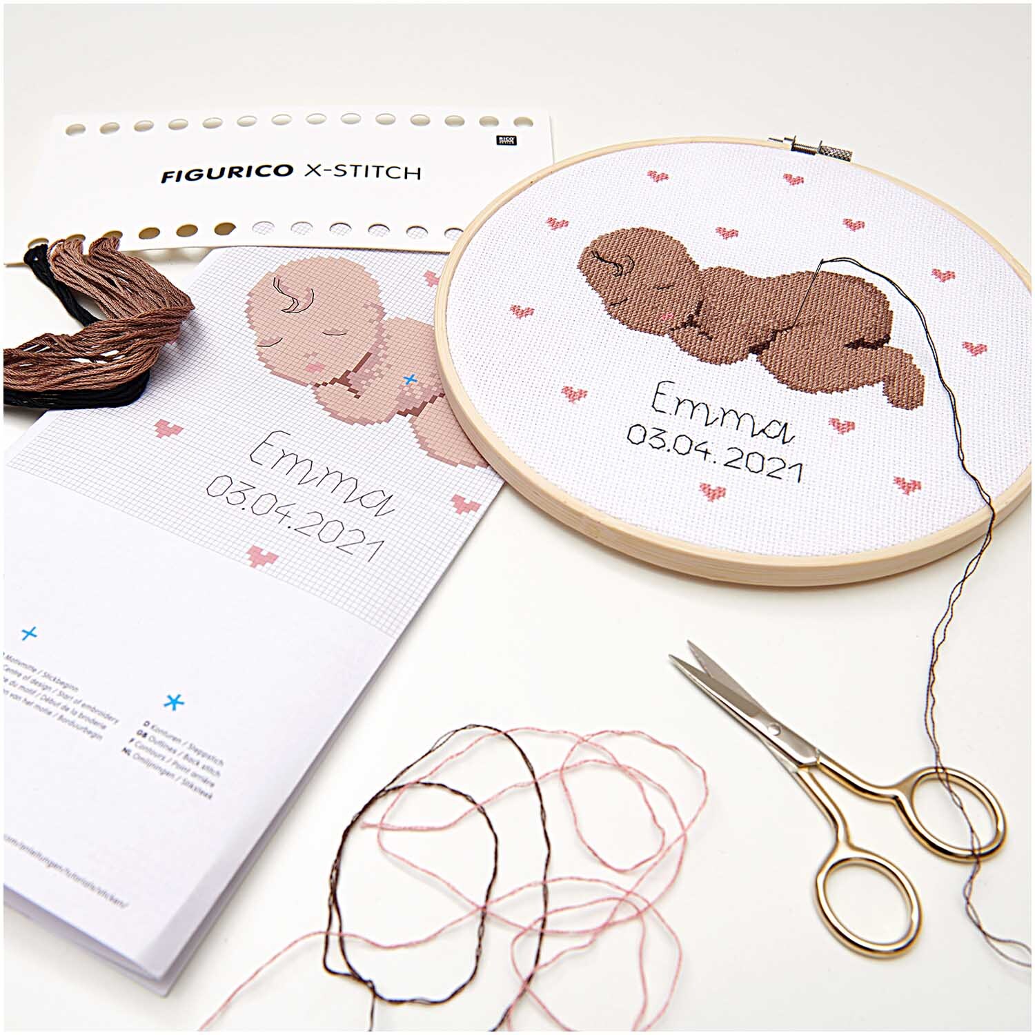 Figurico Stickpackung Baby 20cm zeigt ein gesticktes Baby mit rosa Herzen und Garn auf weißem Stoff.
