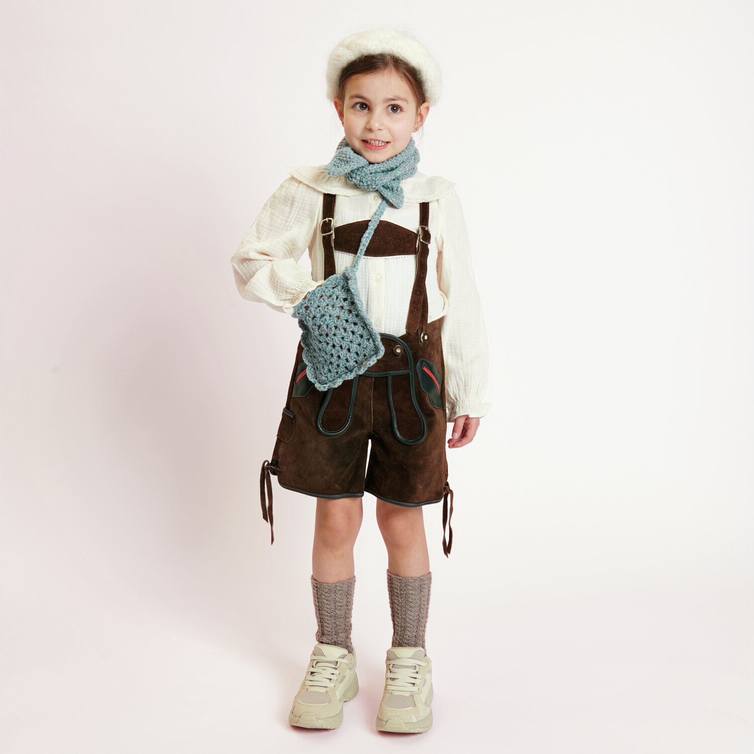 Häkelset Tasche groß Modell 03: Kind in Tracht mit hellbrauner Hose, blauer Tasche und Schal.