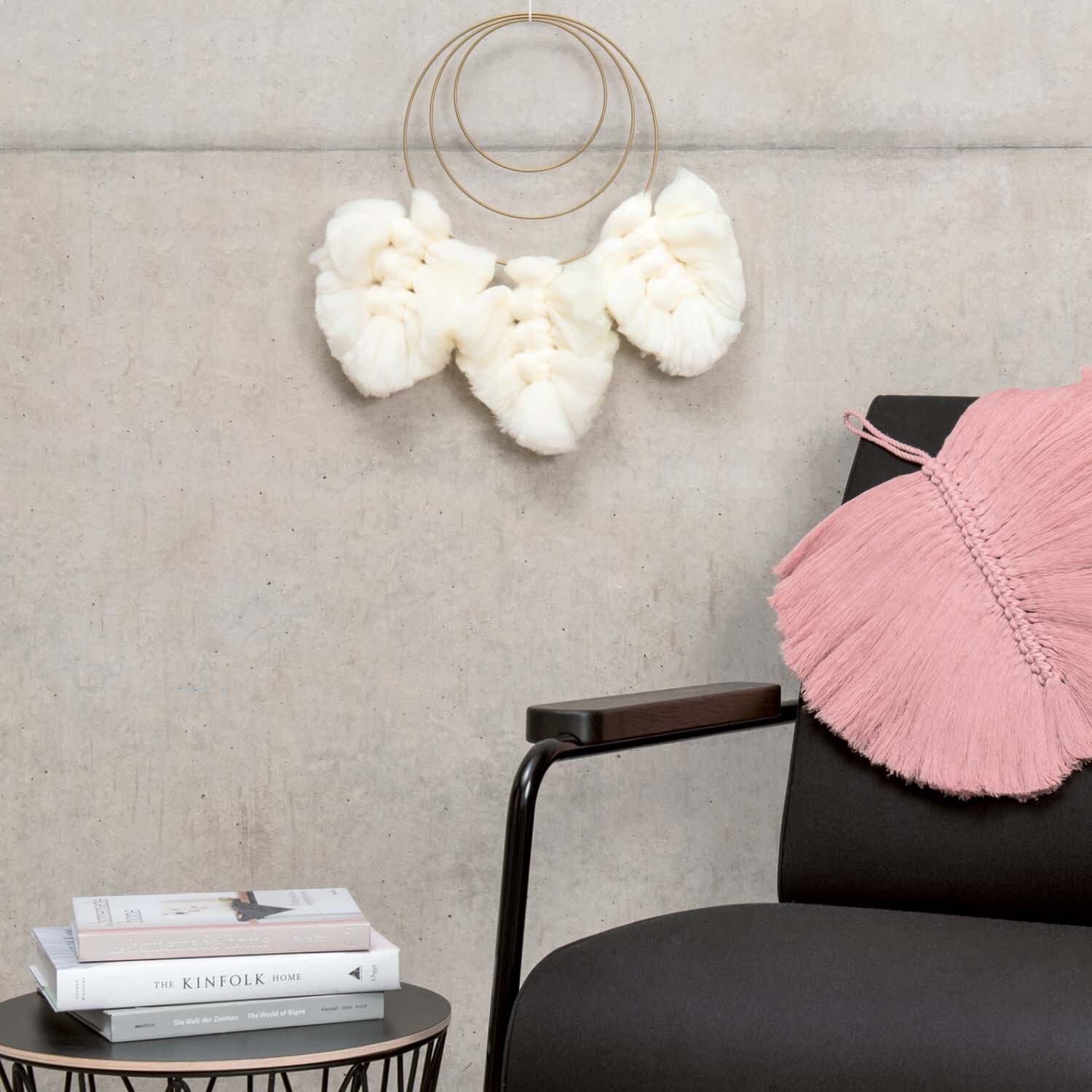 Anleitung Makramee-Blatt knüpfen: Weiße Makramee-Blätter an Wand, neben schwarzem Stuhl mit rosa Kissen.