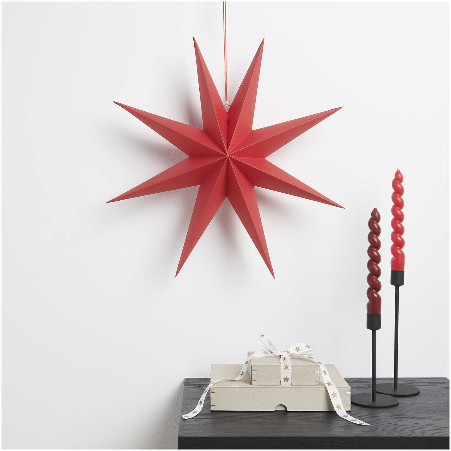 Papierstern auffaltbar 45cm von Rico Design in Rot, dekorativ an der Wand mit Kerzen und Geschenken.