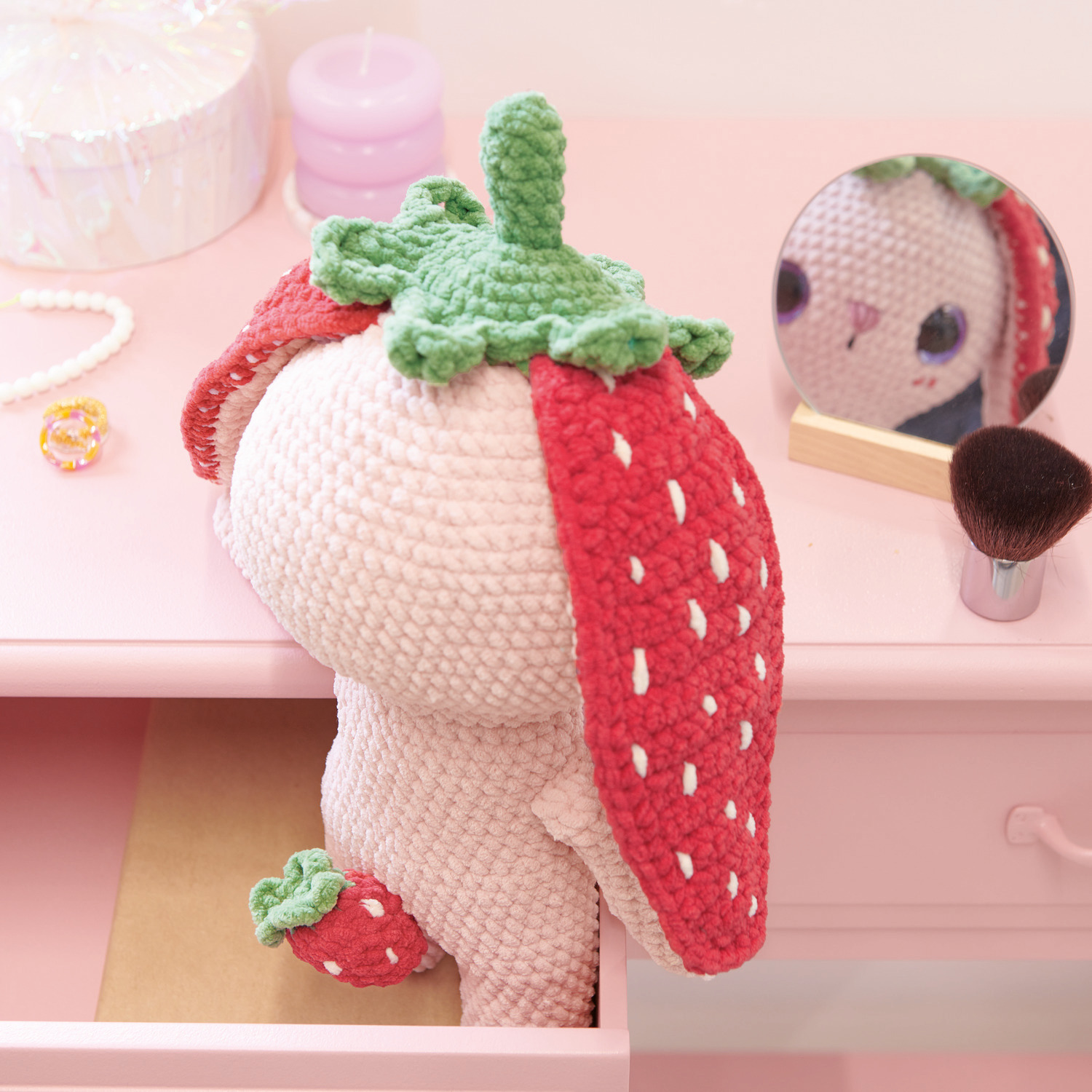 Häkelset Strawberry Bunny Modell 03: Ein gehäkelter Hase mit Erdbeerohren sitzt in einer rosa Schublade.