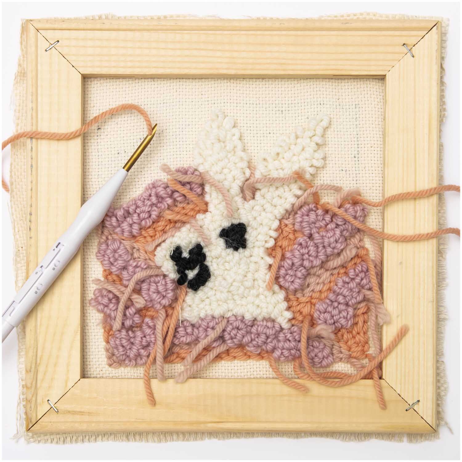 Punch Needle Stickrahmen Holz zeigt ein buntes, handgefertigtes Design in Rosa und Weiß.