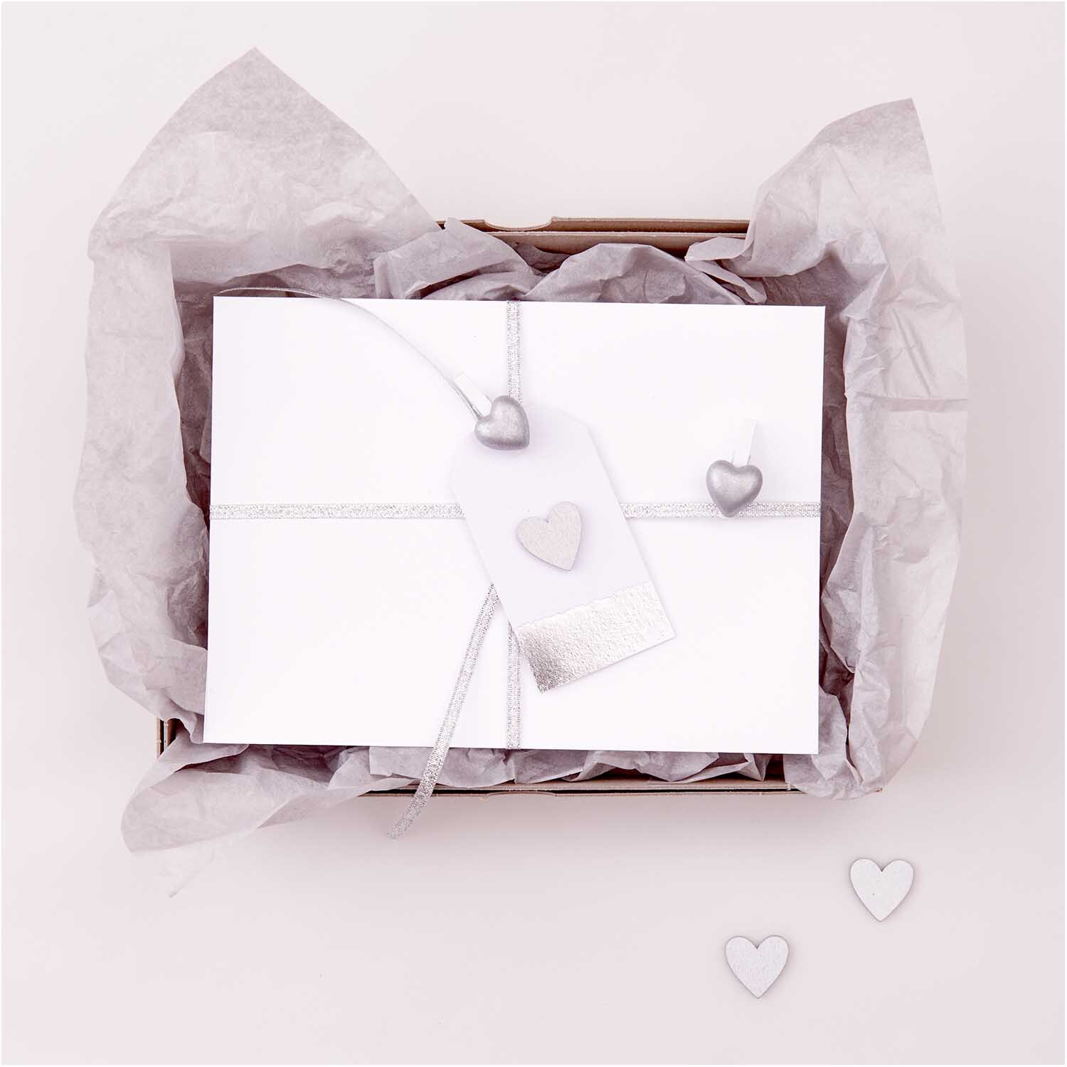 Dekoklammern Herz 8 Stück von Rico Design in Weiß-Silber, dekorativ auf Geschenkbox arrangiert.