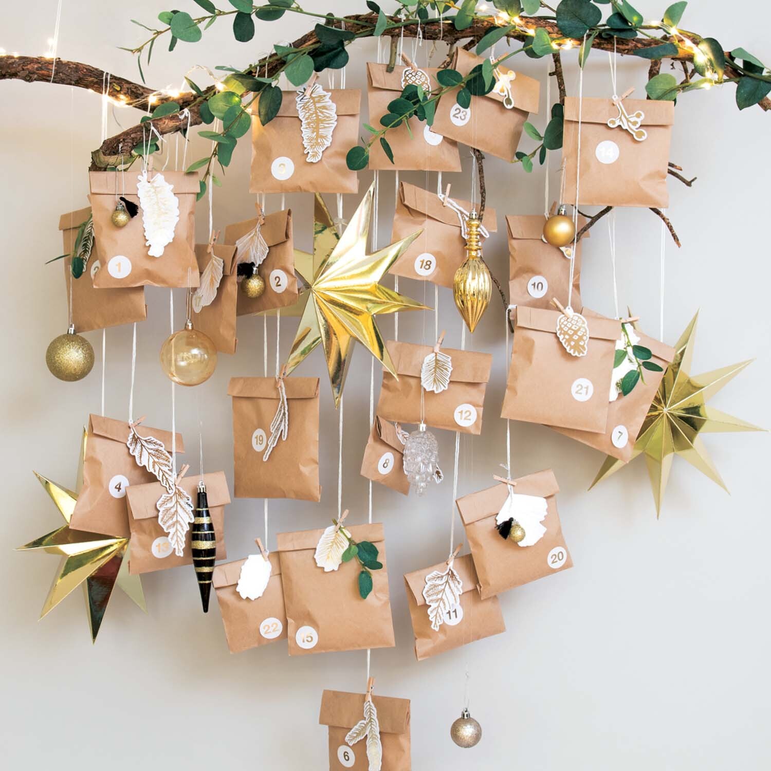 Bastelanleitung Papiertüten-Adventskalender: Ein Ast mit hängenden Papiertüten, goldenen Sternen und Dekorationen.