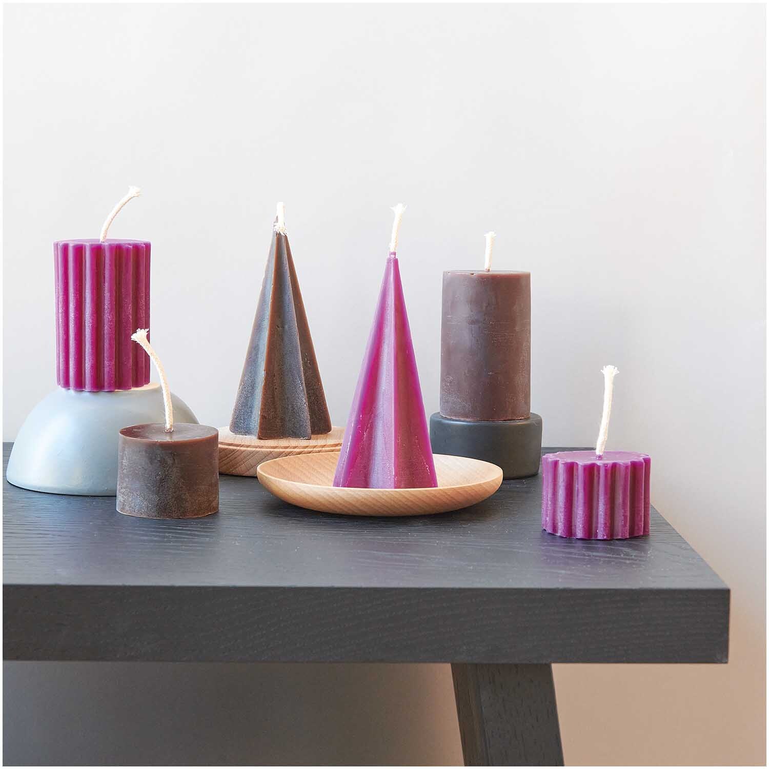 Kerzengießform Sternenkegel 70x70x135mm von Rico Design, umgeben von bunten Kerzen auf einem Tisch.