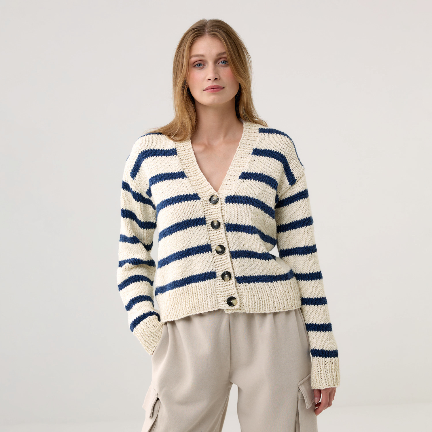 Strickset Jacke Modell 21: Frau trägt gestreifte Strickjacke mit Knöpfen, beige und blau, lässiger Stil.