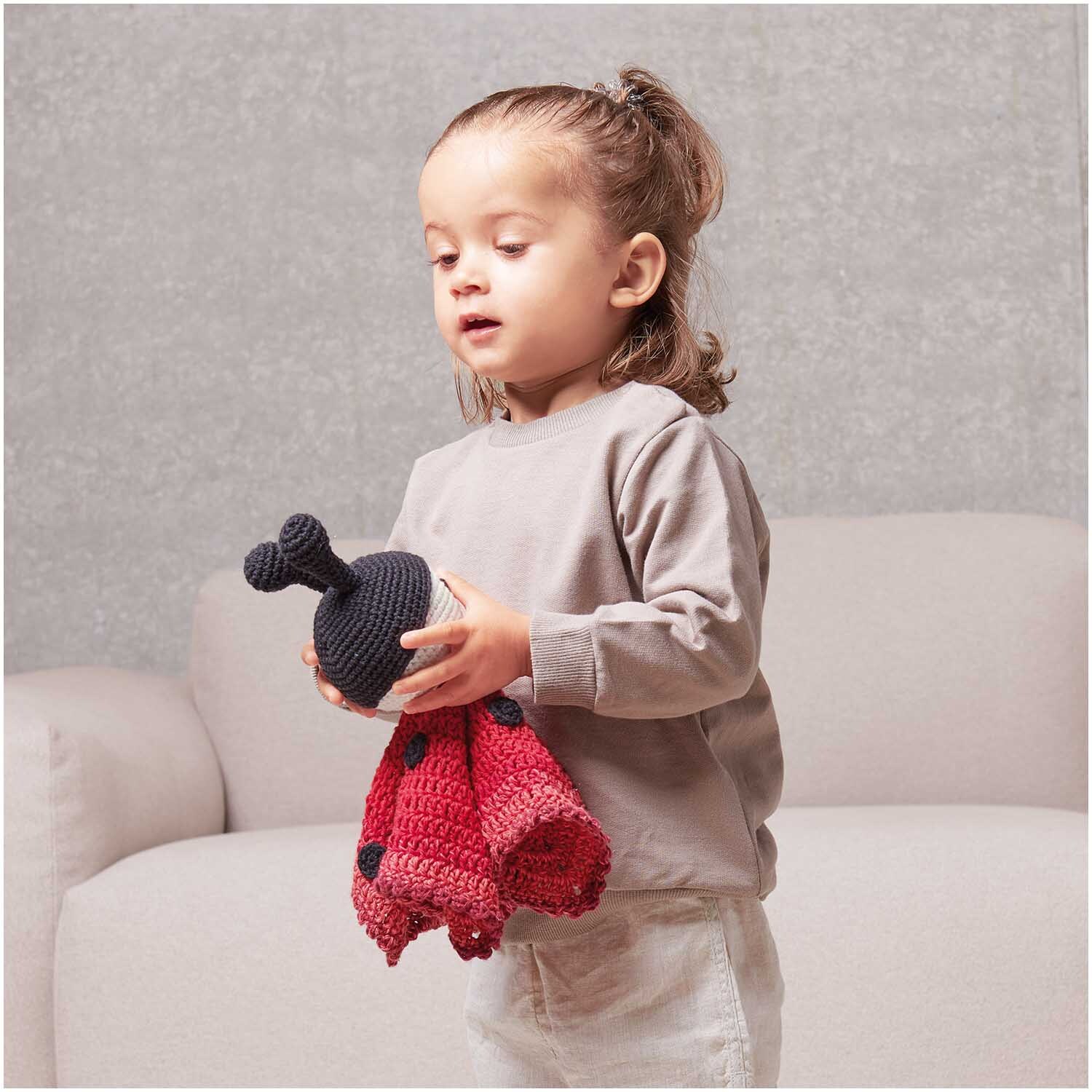 Häkelset Ricorumi Baby Blankies Marienkäfer: Kind hält ein rotes, gehäkeltes Marienkäfer-Spielzeug von Rico Design.