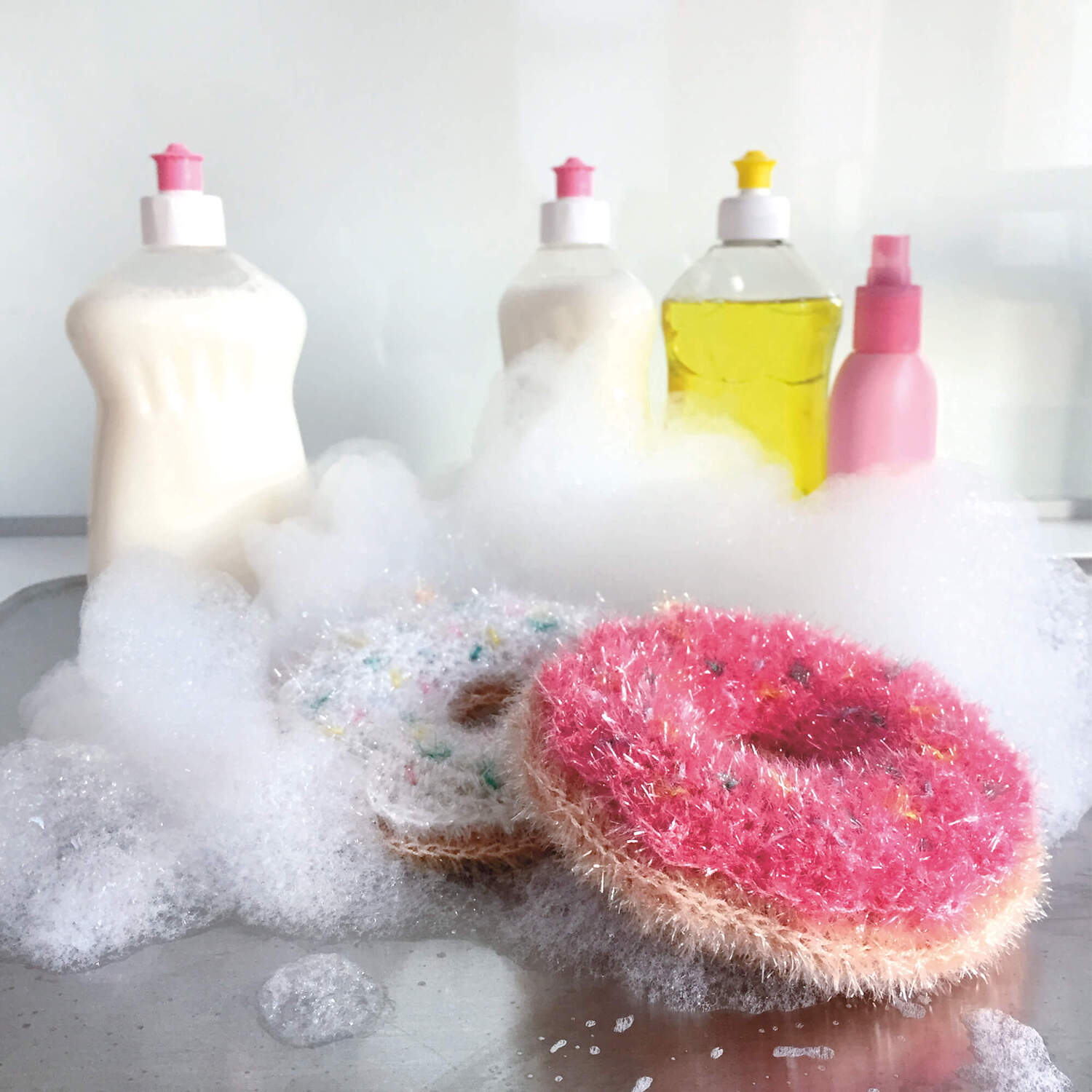 Häkelanleitung Donut Spülschwamm aus Creative Bubble, umgeben von Schaum und Spülmittelflaschen.