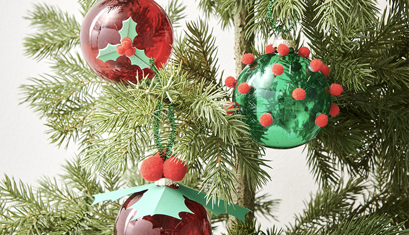 Bastelanleitung Baumschmuck in klassischen Farben: Rote und grüne Kugeln mit Dekoration an einem Tannenbaum.