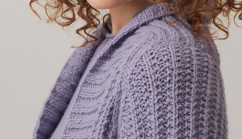 Strickanleitung Damenjacke aus Creative Soft Wool aran: Frau trägt lila gestrickte Jacke mit detailliertem Muster, ideal für kühle Tage.
