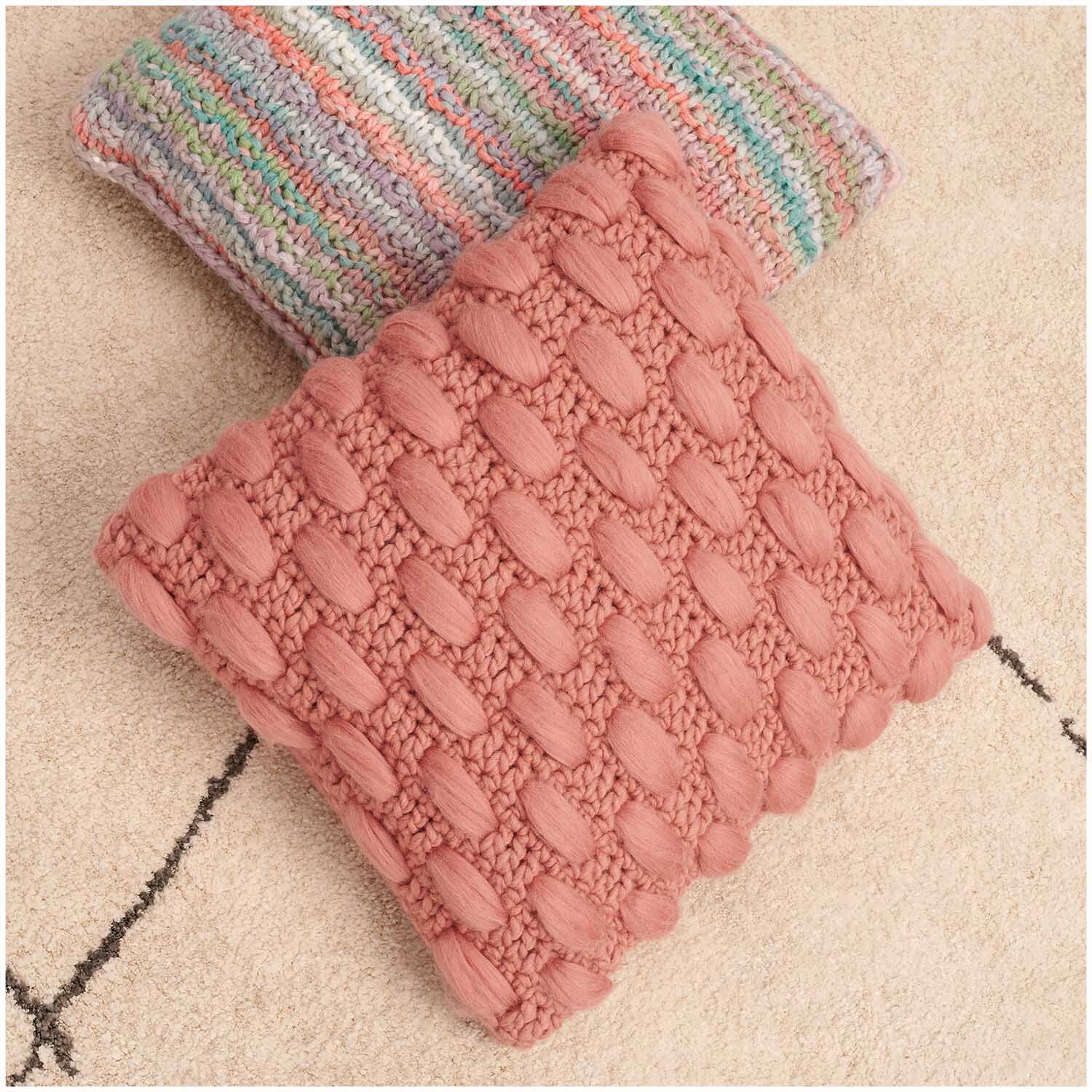 Creative Cocon Kissen in Altrosa mit strukturierter Strickoptik auf beigem Teppich. Ideal für gemütliche Wohnräume.