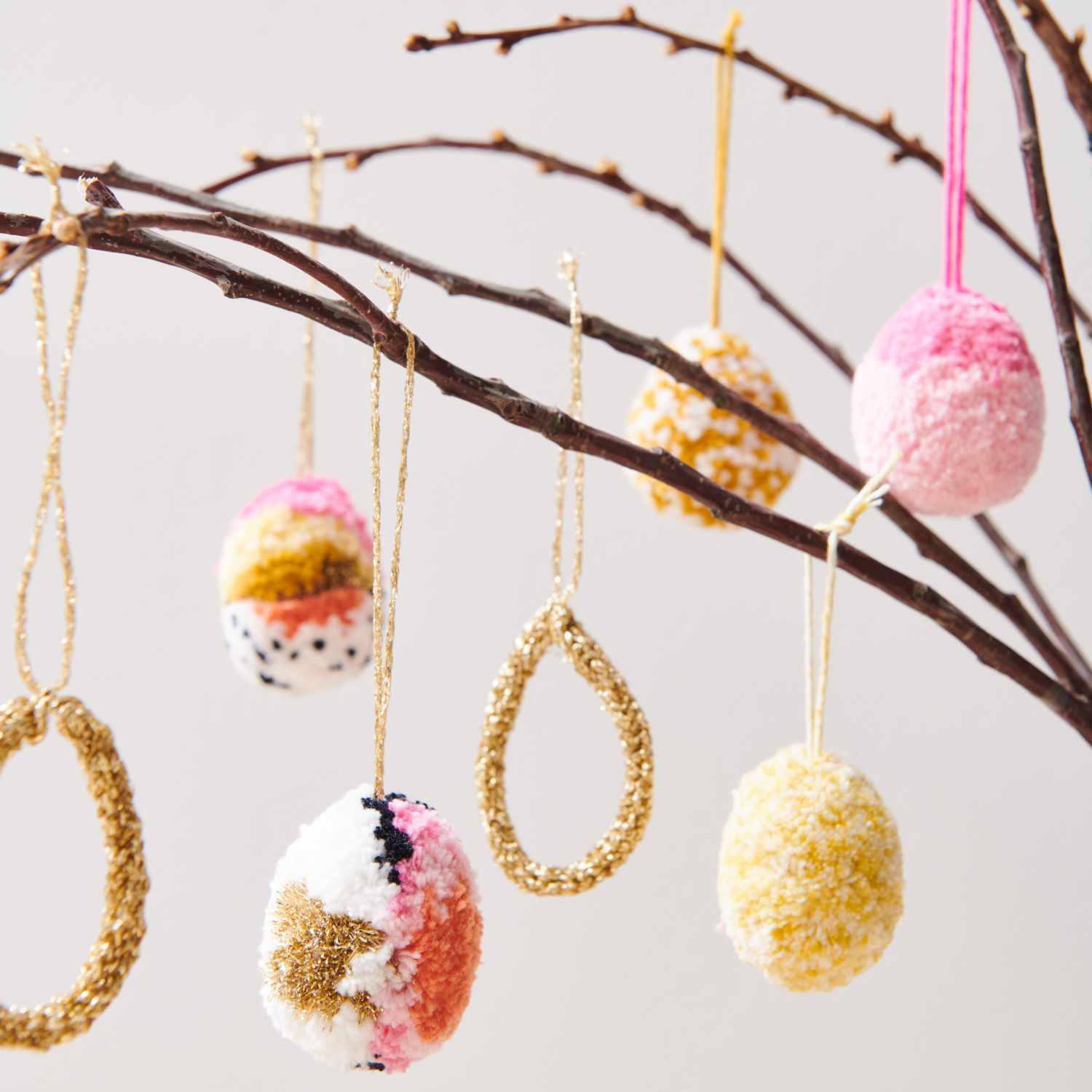 Bastelanleitung Pomponeier: Bunte Pompon-Ostereier und goldene Ringe hängen an Zweigen.