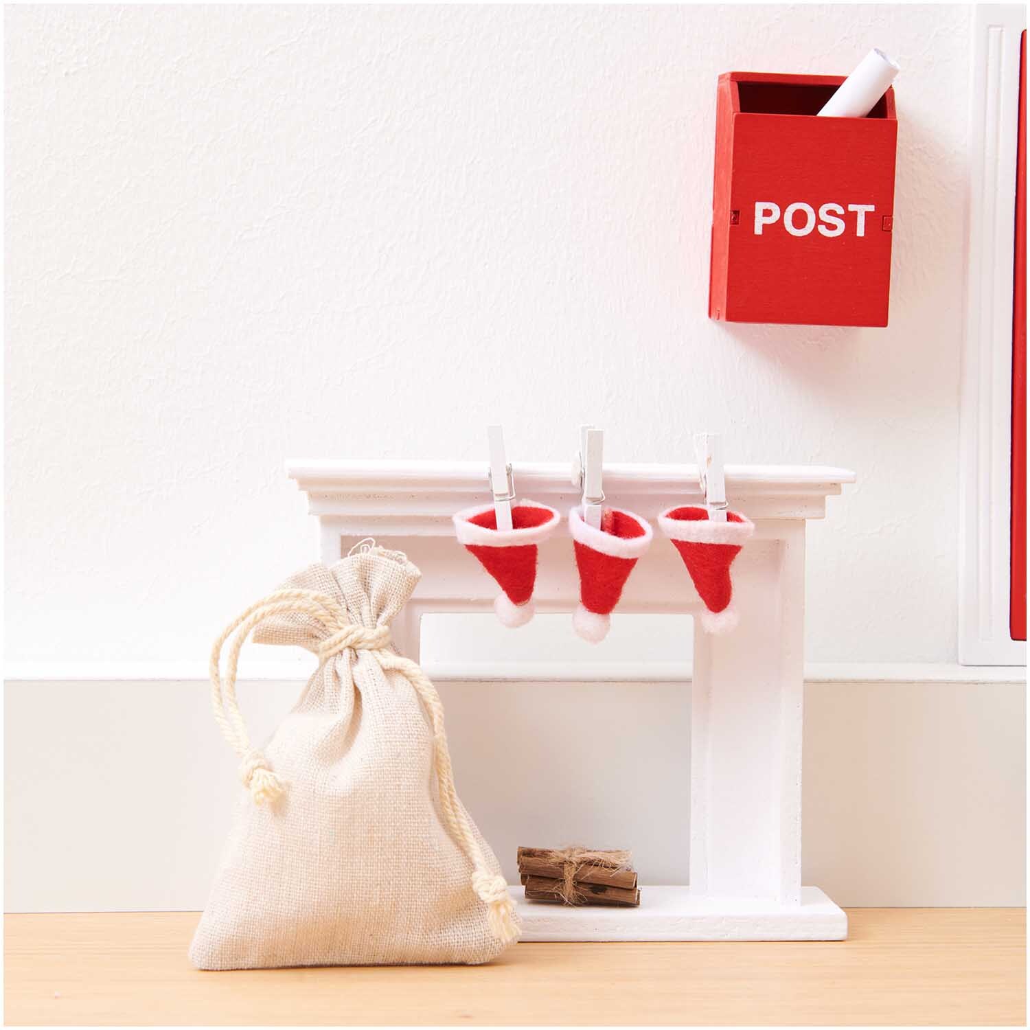 Wichtelwelt Deko Set Nikolaus: Ein weißes Regal mit roten Nikolausmützen, einem Postsack und rotem Briefkasten von Rico Design.
