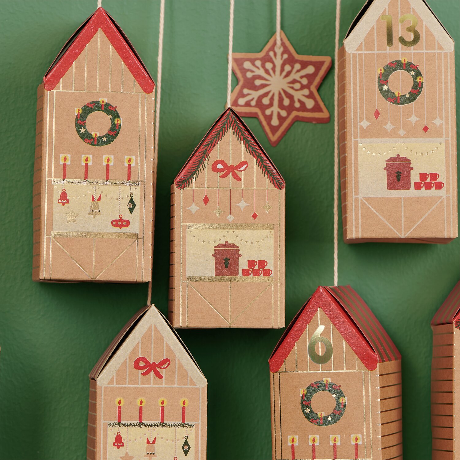 Adventskalender Bastelset: Hängende Häuser aus Karton mit roten Dächern und weihnachtlichen Motiven.