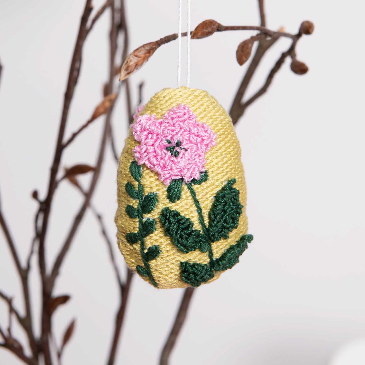 Anleitung Osteranhänger mit Punch Needle: Gelber Anhänger mit rosa Blume und grünen Blättern an Zweigen.