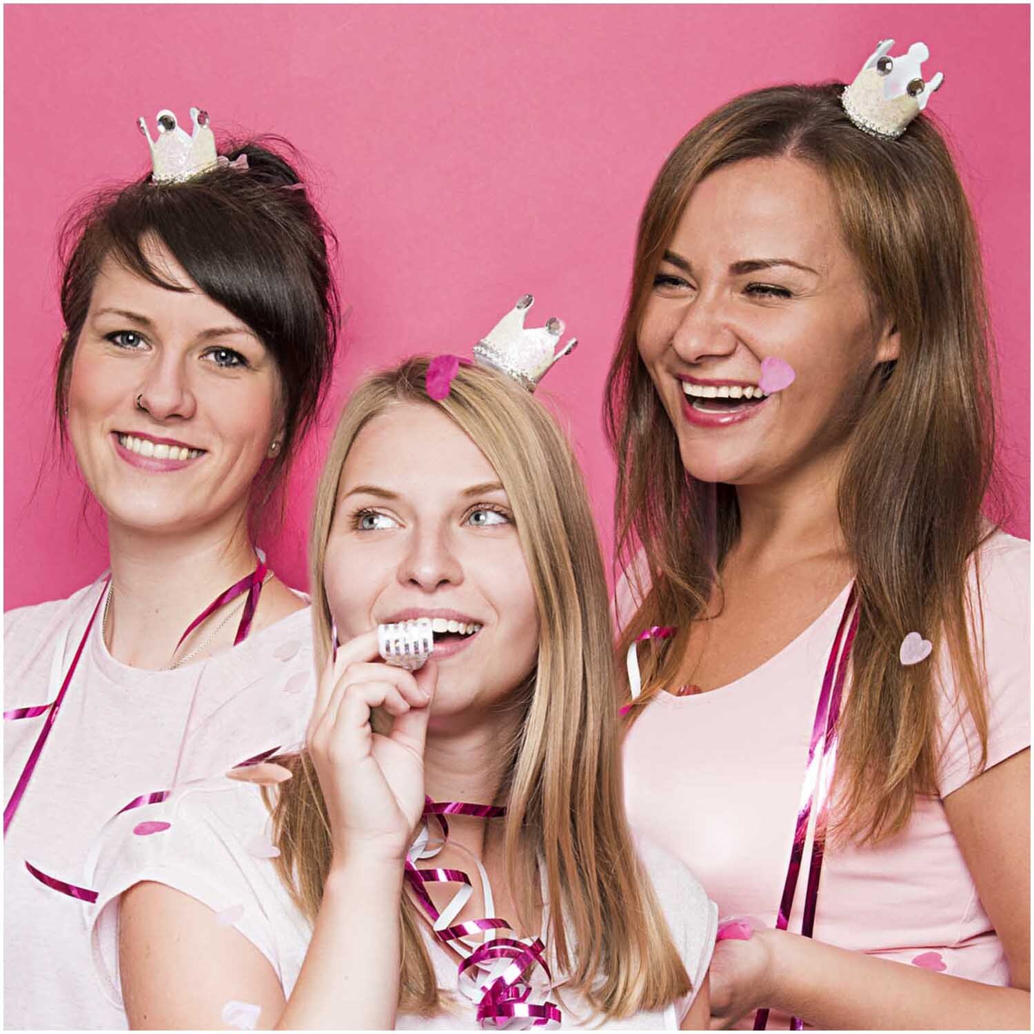 Partykronen 4,5x5cm 6 Stück: Drei lachende Frauen tragen weiße Kronen von Rico Design vor rosa Hintergrund.