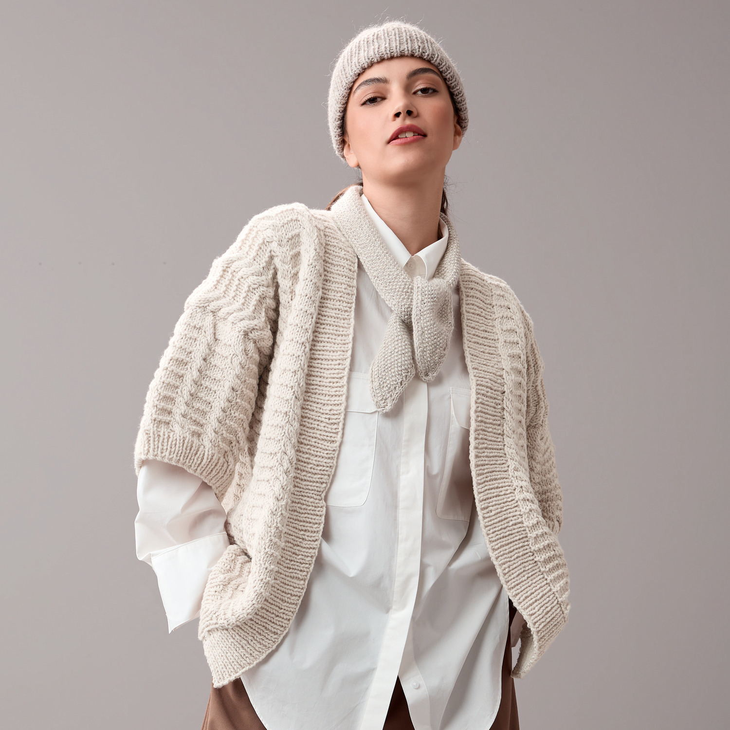 Baby Alpaka: Frau trägt beige Strickjacke und Mütze, kombiniert mit weißer Bluse, stilvoll und elegant.