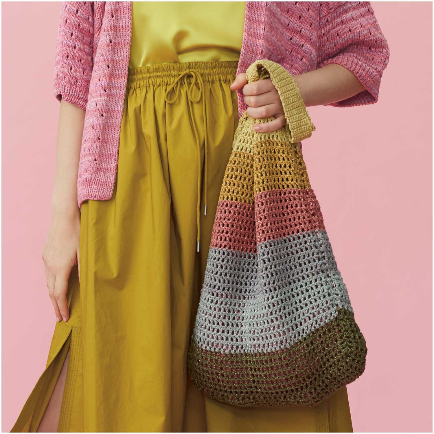 Fashion Cotton Métallisé dk: Frau mit bunter Häkel-Tasche, gelbem Rock und rosa Strickjacke vor rosa Hintergrund.